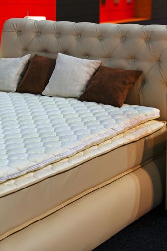 Una testiera trapuntata beige su un letto con un coprimaterasso trapuntato bianco e cuscini decorativi marroni e bianchi.