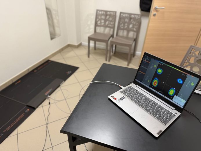 In una stanza con due sedie, un computer portatile su una scrivania visualizza i dati biometrici provenienti da un tappetino sensibile alla pressione posizionato sul pavimento.
