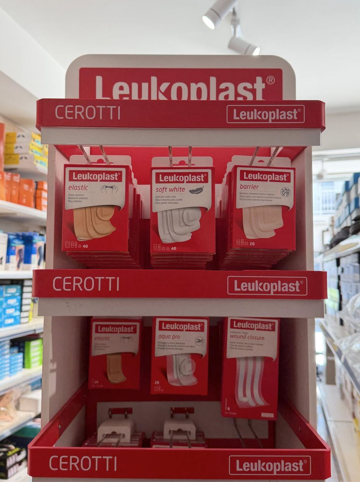 Uno scaffale espositivo in un negozio, con diverse confezioni di cerotti adesivi del marchio Leukoplast.