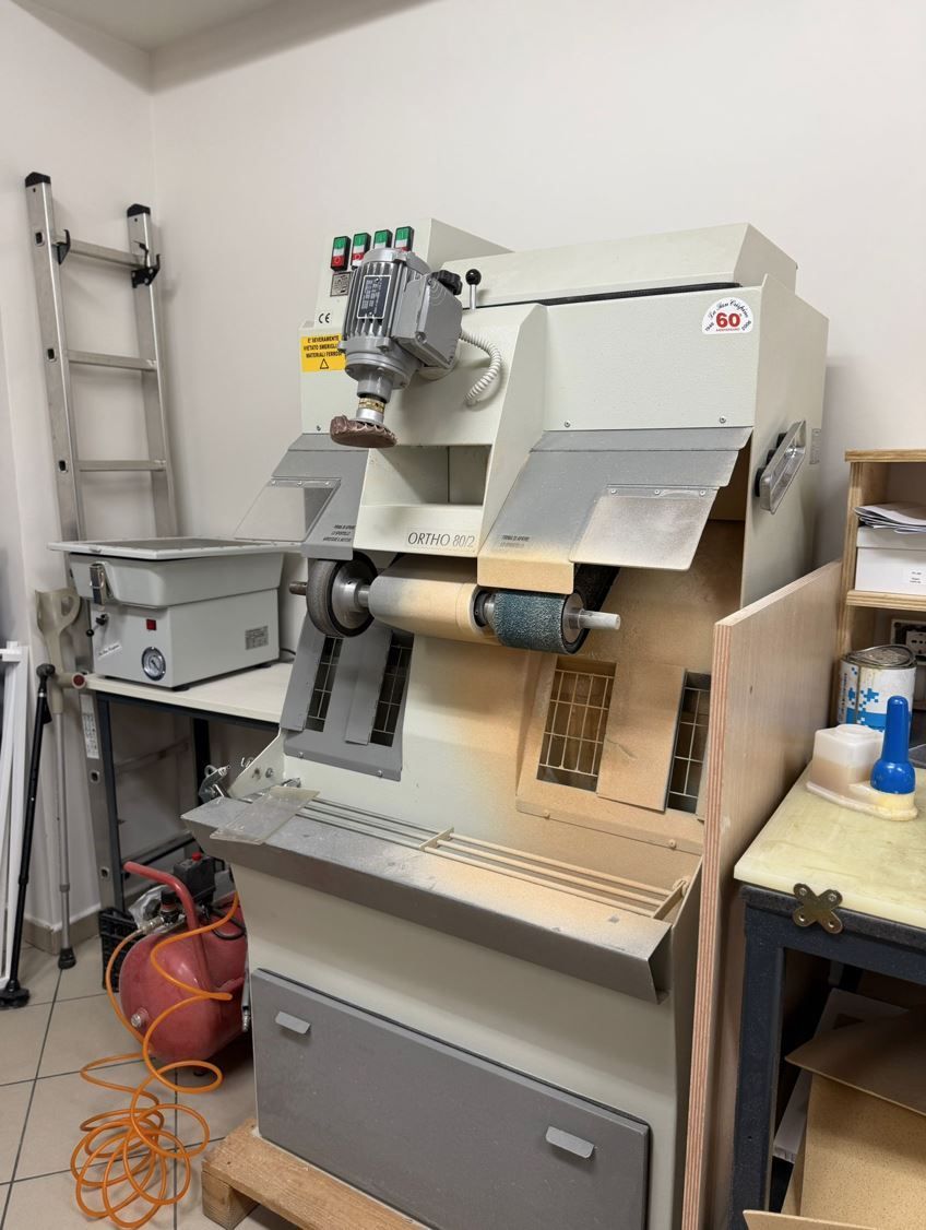 In un'officina, accanto a una scala e ad altre attrezzature, si trova una macchina industriale di colore chiaro 