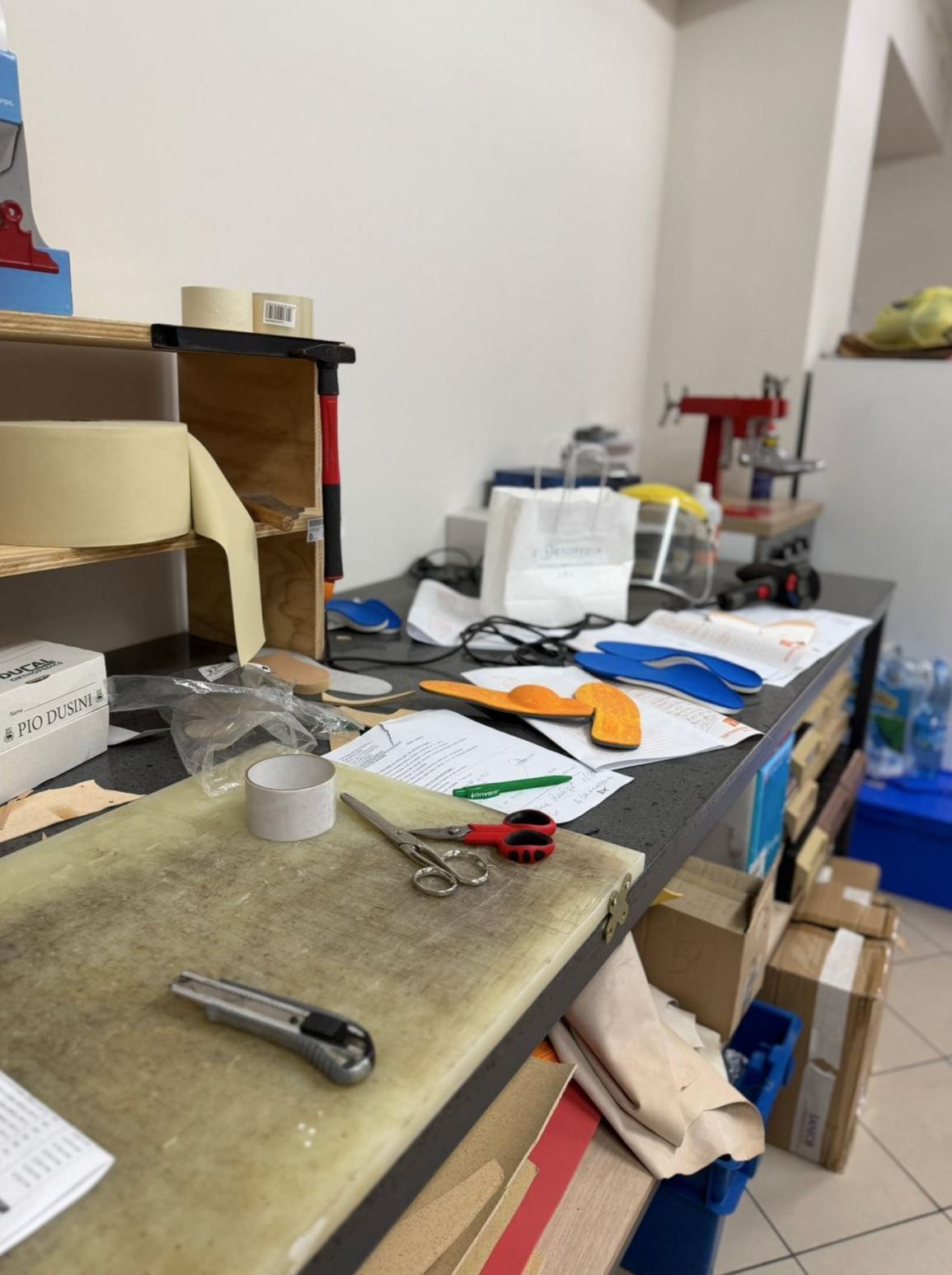 Un banco da lavoro ingombro di attrezzi da taglio, nastro adesivo, modelli di carta e materiali per il bricolage.