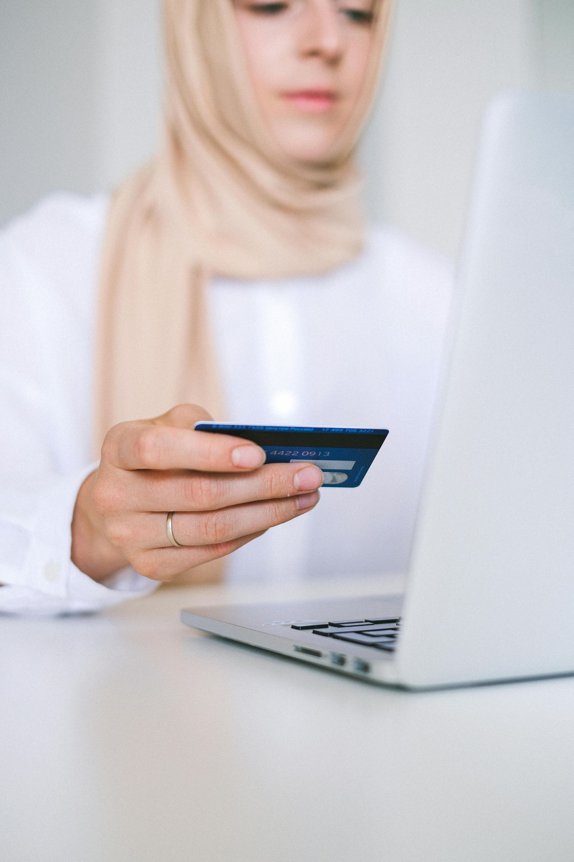 Mulher de hijab segurando cartão de crédito e usando laptop para fazer compras online.