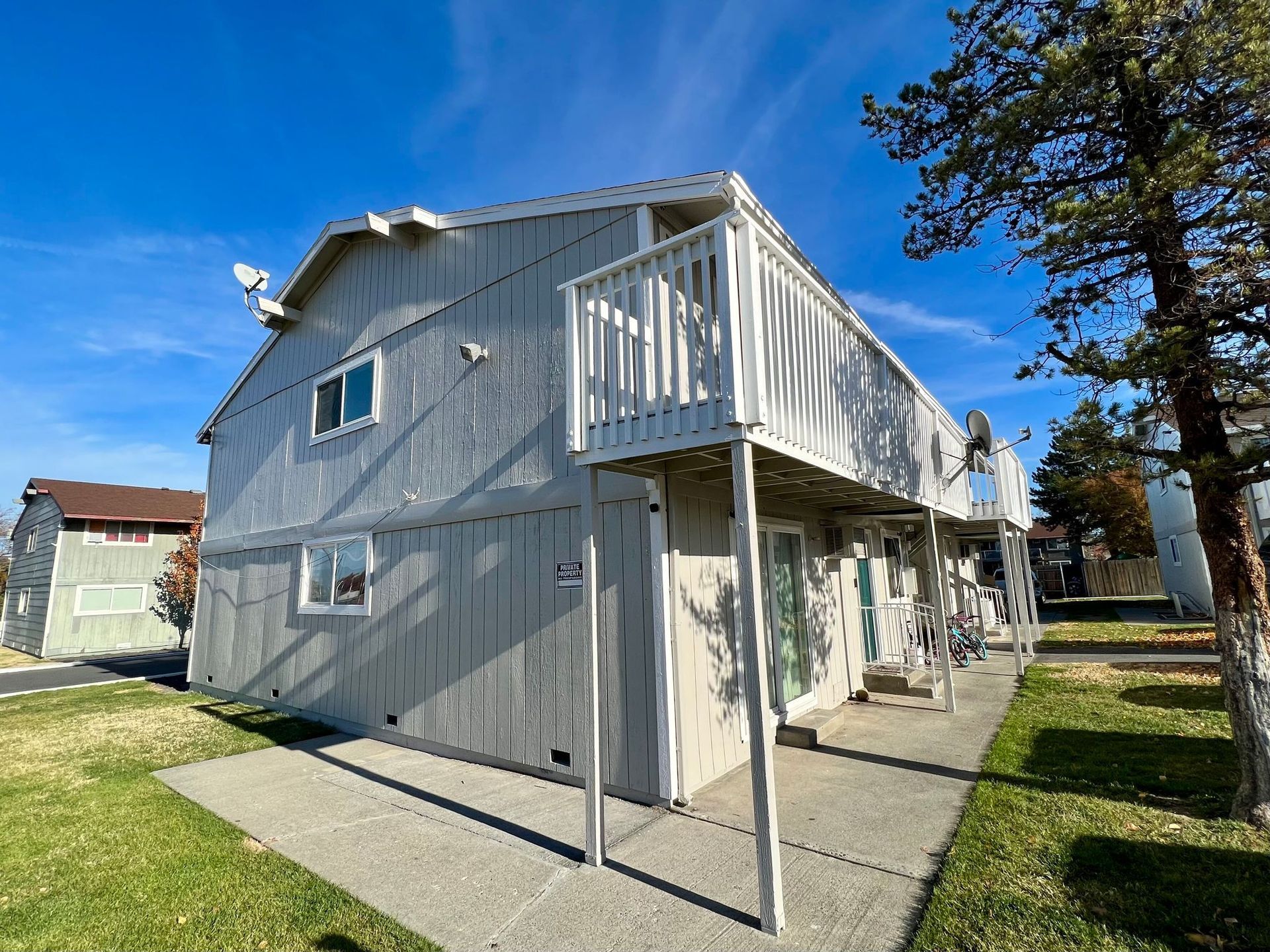 White two-story house with a small balcony and covered walkway under a bright blue sky