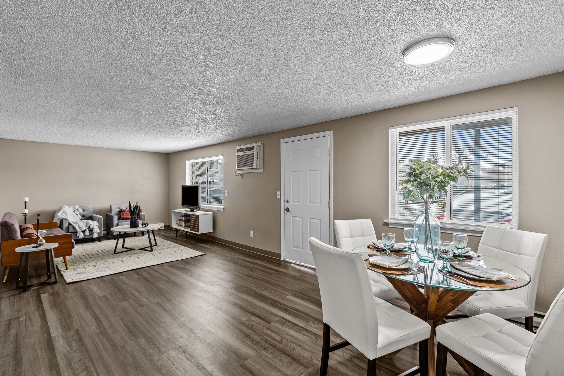 Bright open dining and living room with white table, chairs, sofa, and wood floors near a window.