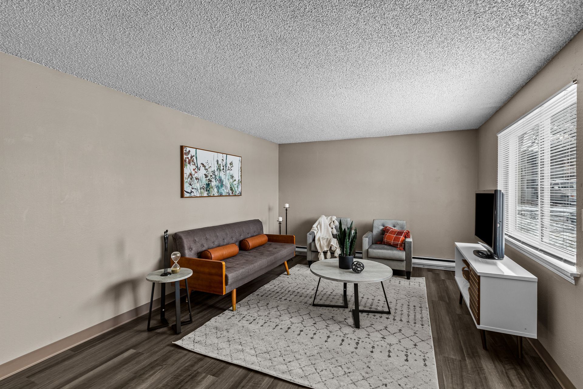 Modern living room with a sofa, coffee table, rug, and large windows with blinds