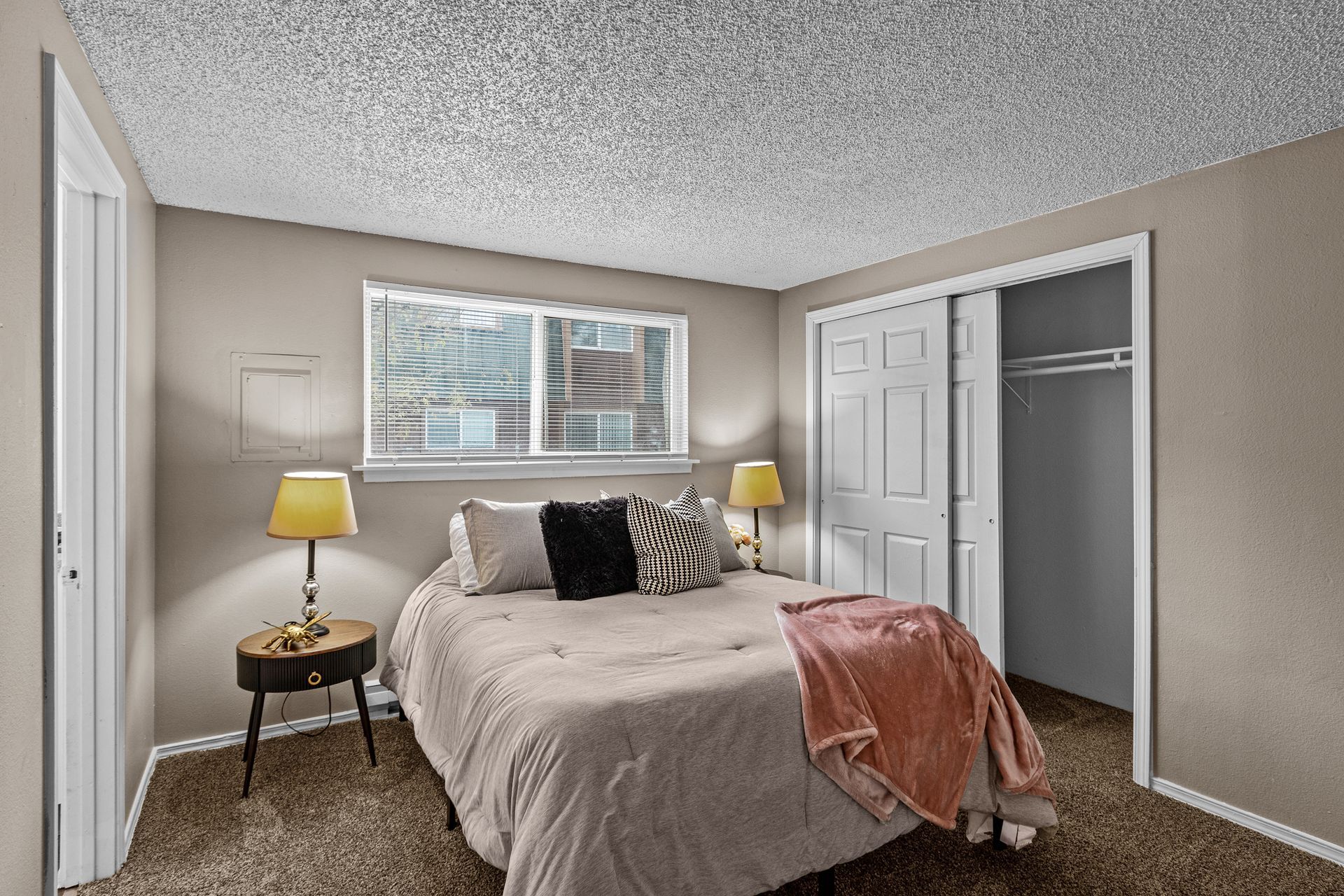 Cozy bedroom with a bed, two bedside lamps, window, and open closet doors.