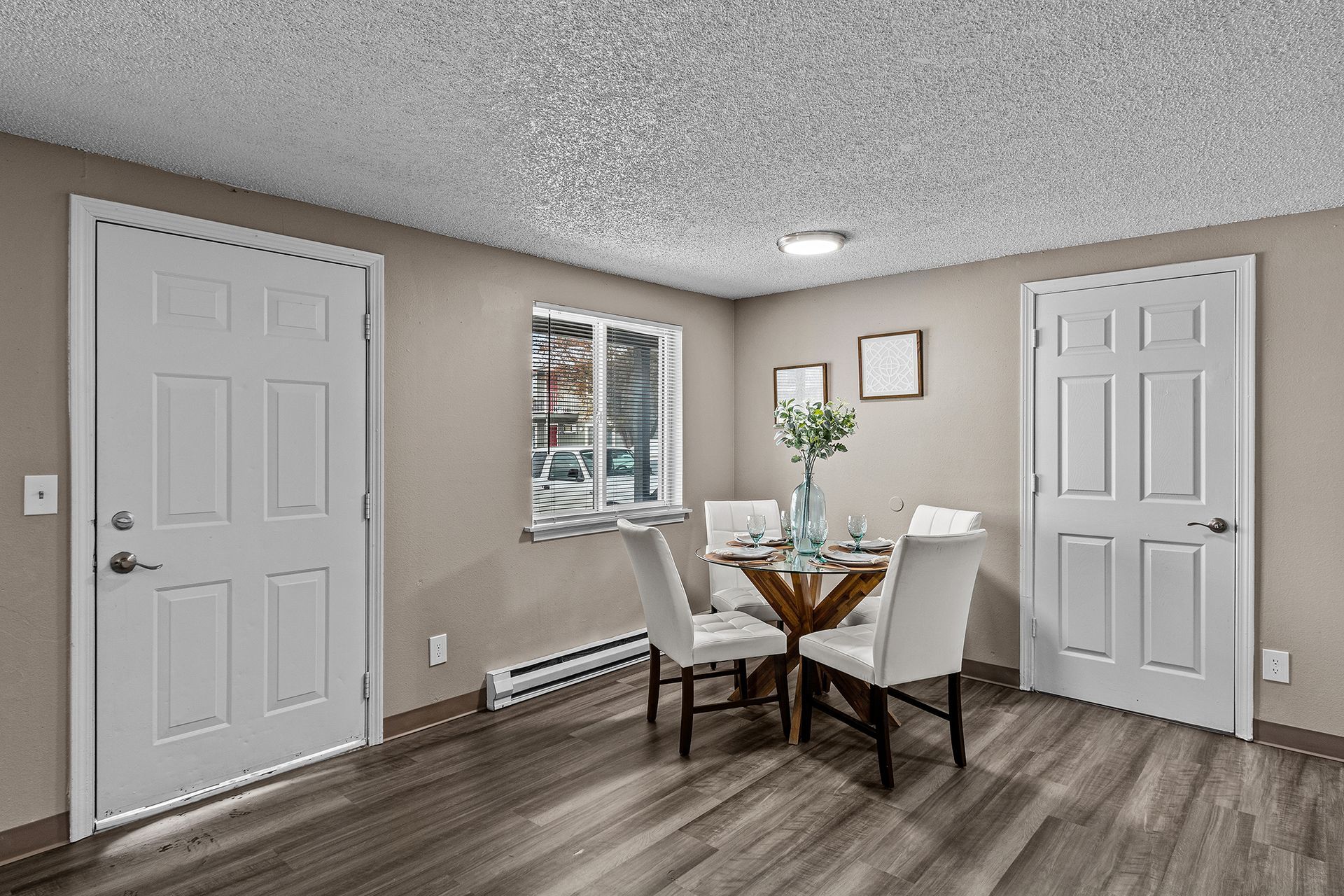 Small dining area with table and chairs, white doors, window, and gray walls in a modern room
