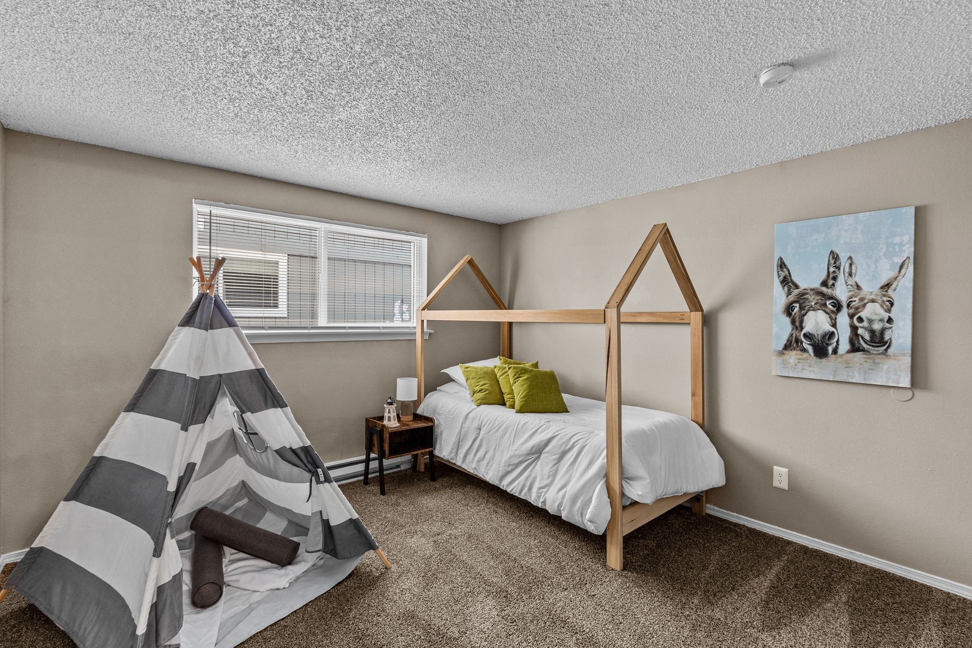 Child’s bedroom with a teepee, wooden house bed, striped bedding, and giraffe wall art
