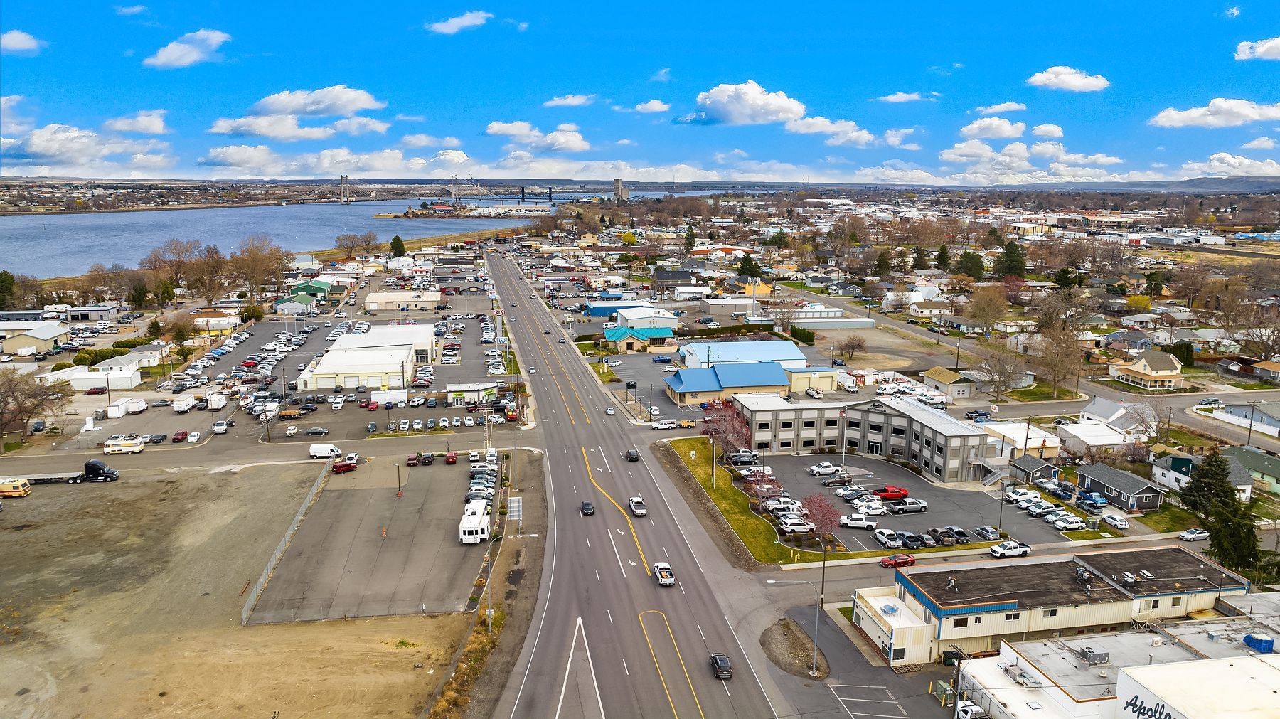 Aerial view of a coastal town with a main road, buildings, and water in the distance under a cloudy sky