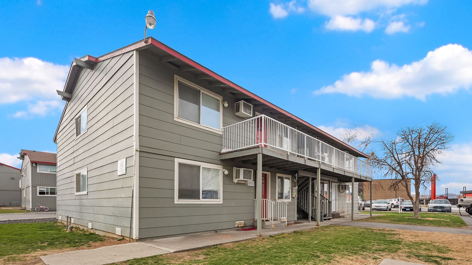 Gray two-story apartment building with red roof trim and a covered front porch on a cloudy day