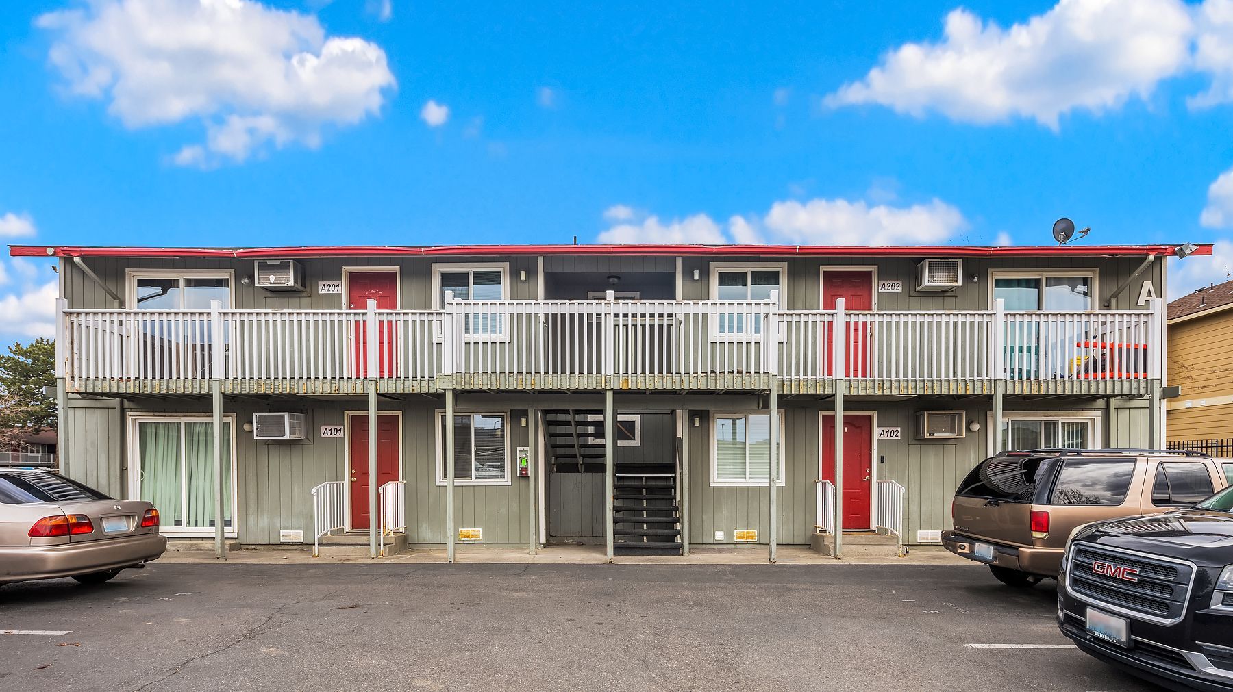 Two-story motel with red roof and balconies, parked cars in front under a blue sky.