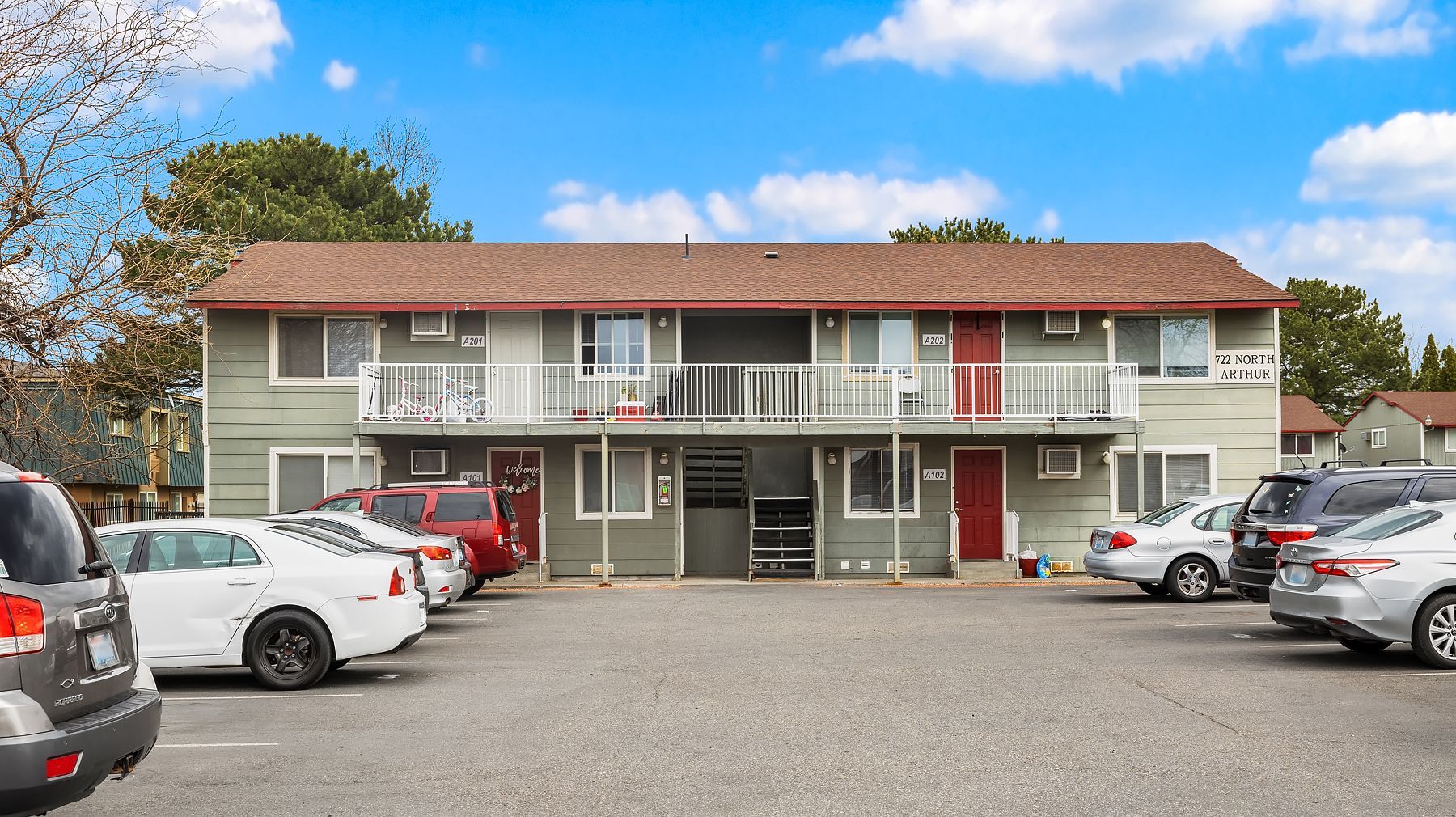 Motel-style two-story building with parked cars in front under a partly cloudy sky