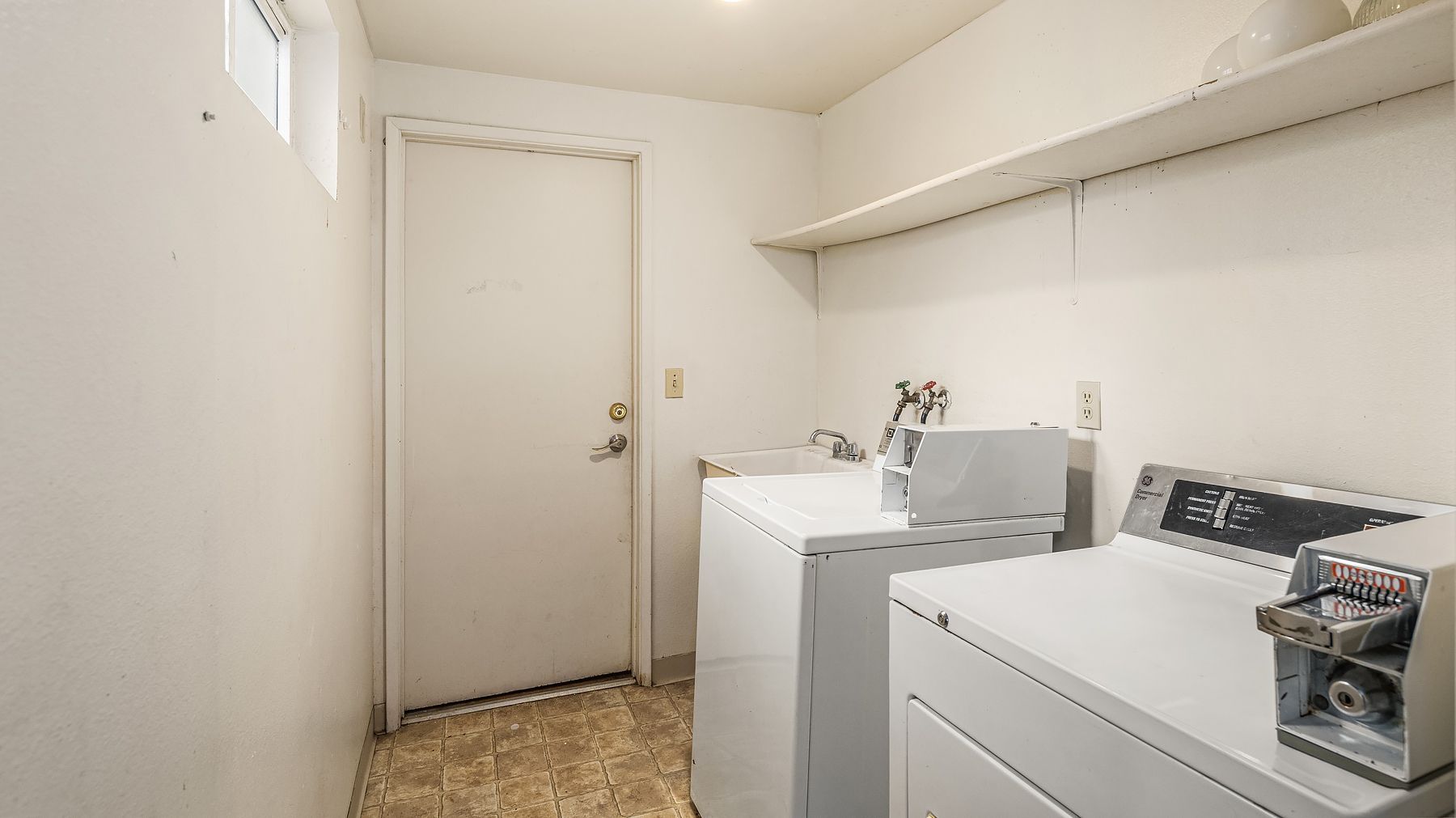 Small laundry room with washer, dryer, utility sink, and a closed door on the left.