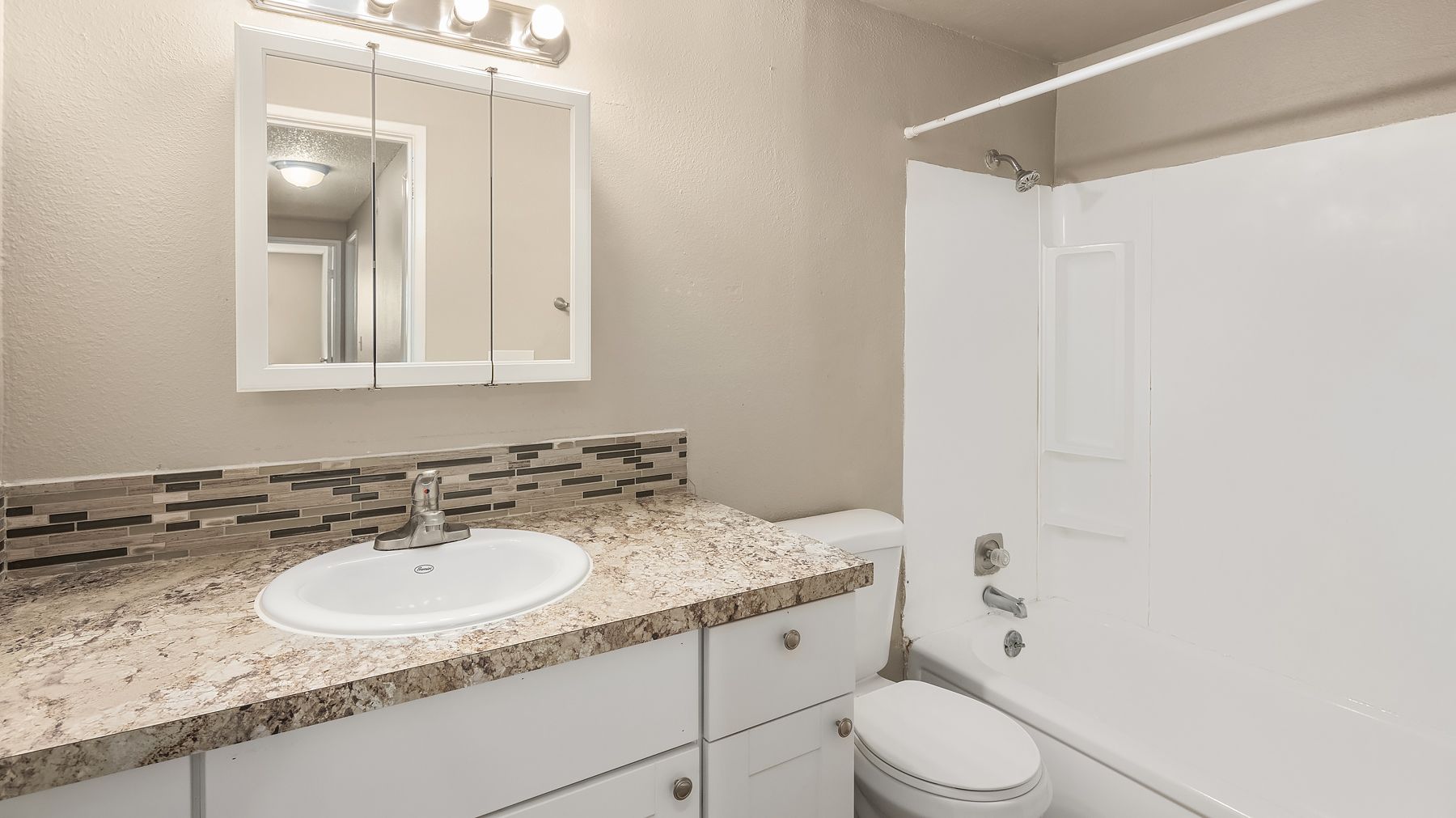 Bathroom with granite vanity, oval sink, mirror cabinet, and white tub-shower surround.