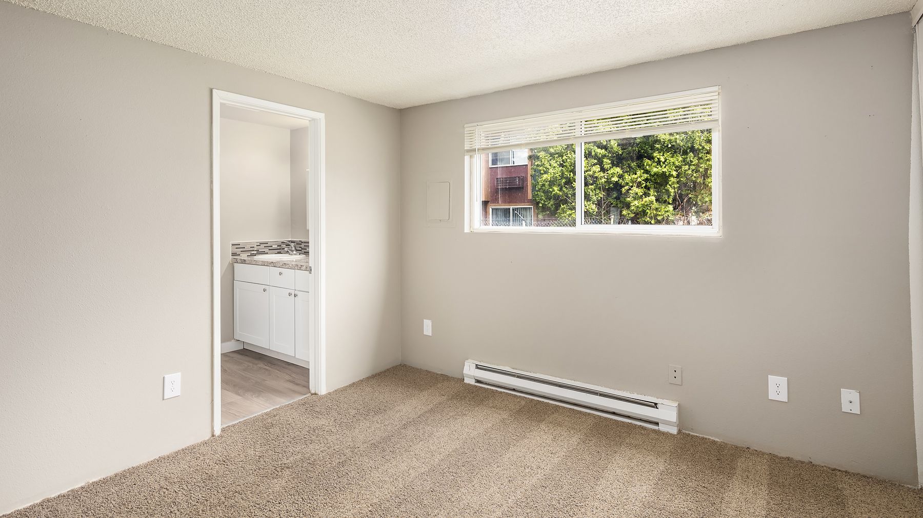 Empty beige bedroom with carpet, small window, and open doorway to a bathroom.