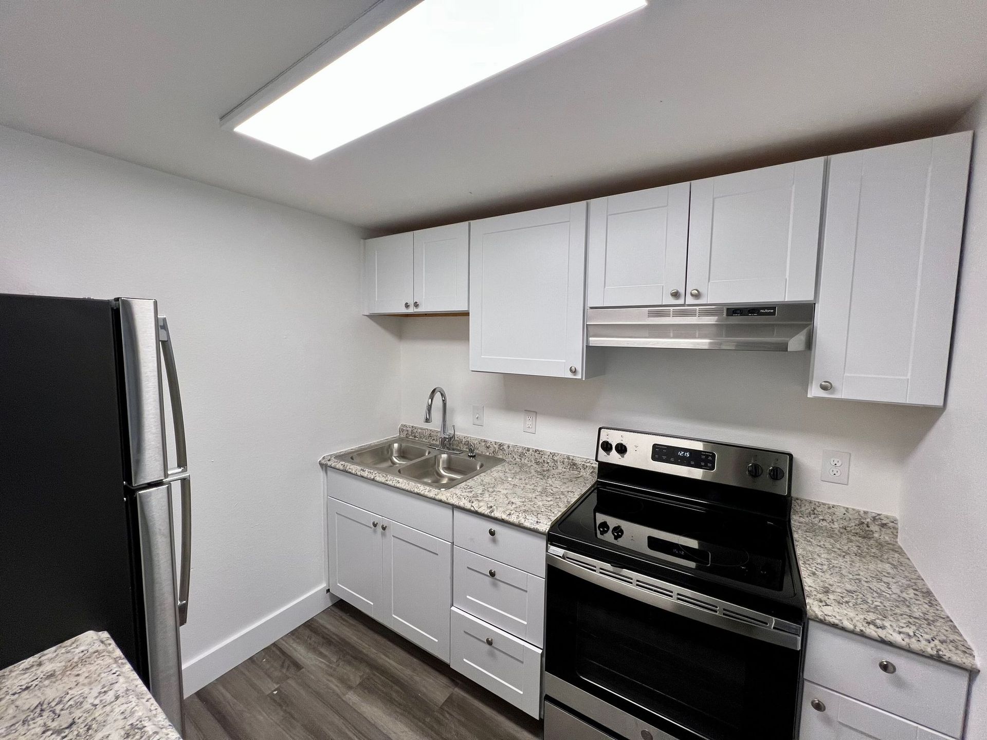 Small white kitchen with black appliances, white cabinets, and speckled granite countertops.