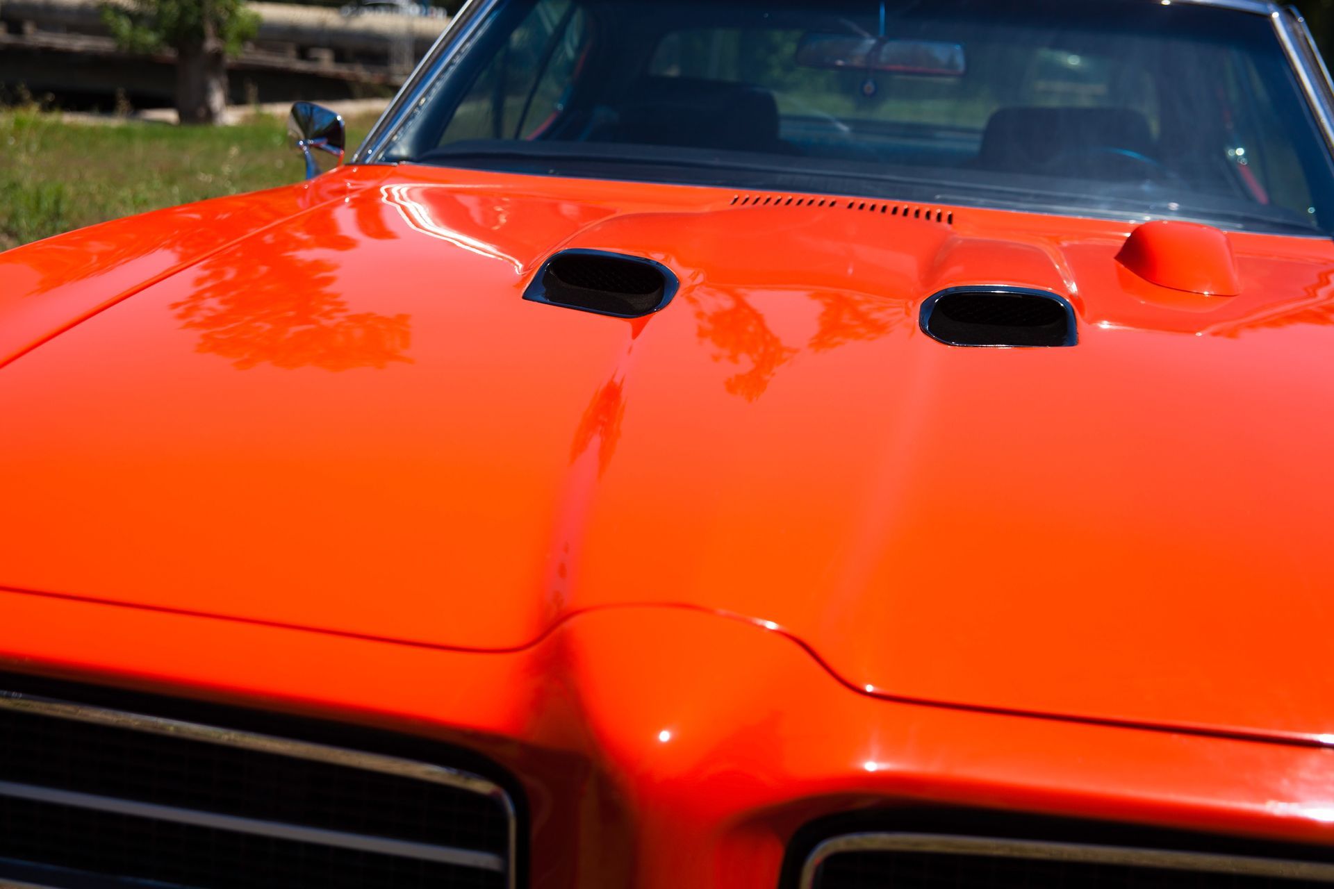A close up of the hood of an orange car with a hood scoop.