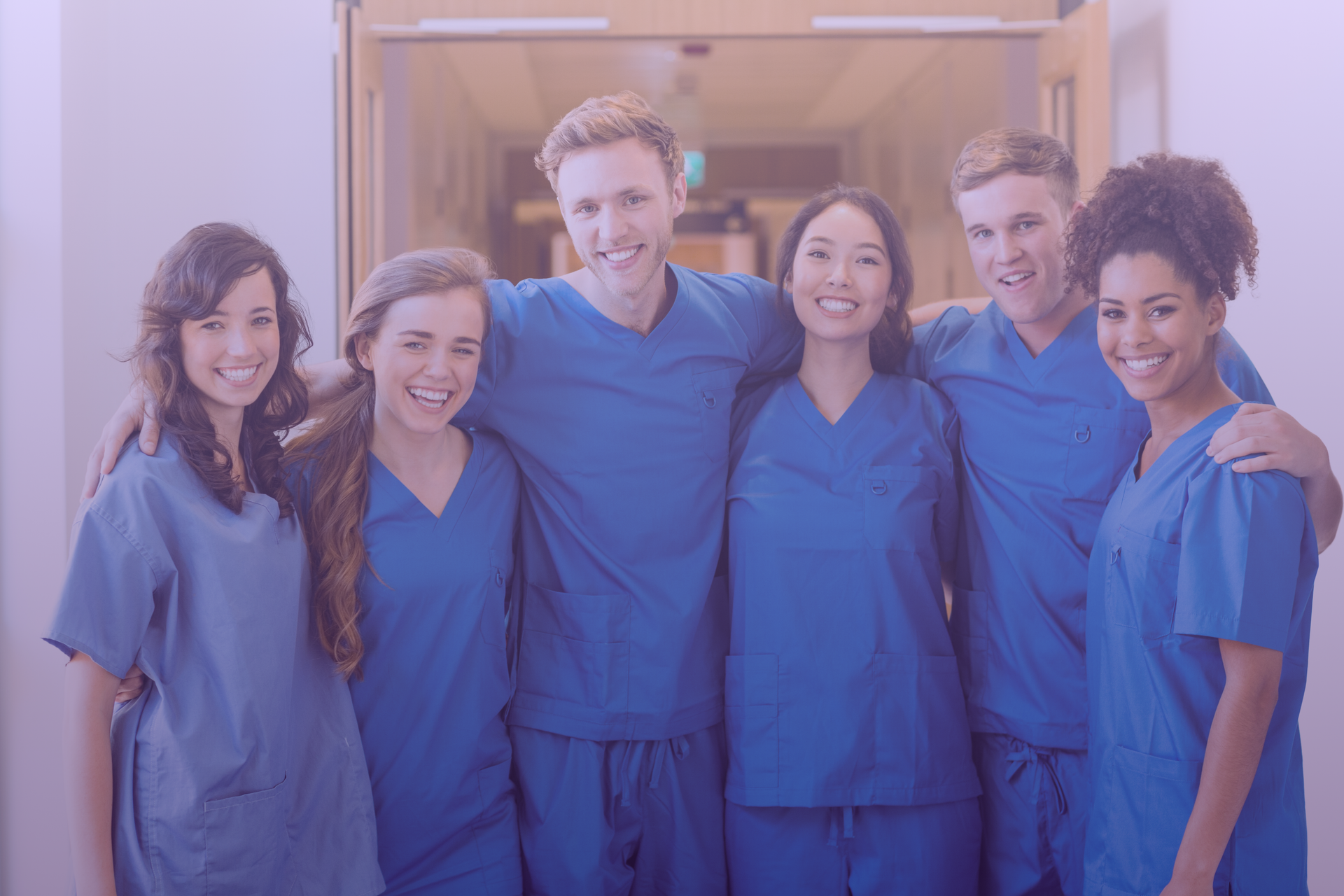 Medizinisches Personal in blauer OP-Kleidung lächelt und posiert in einem Flur.