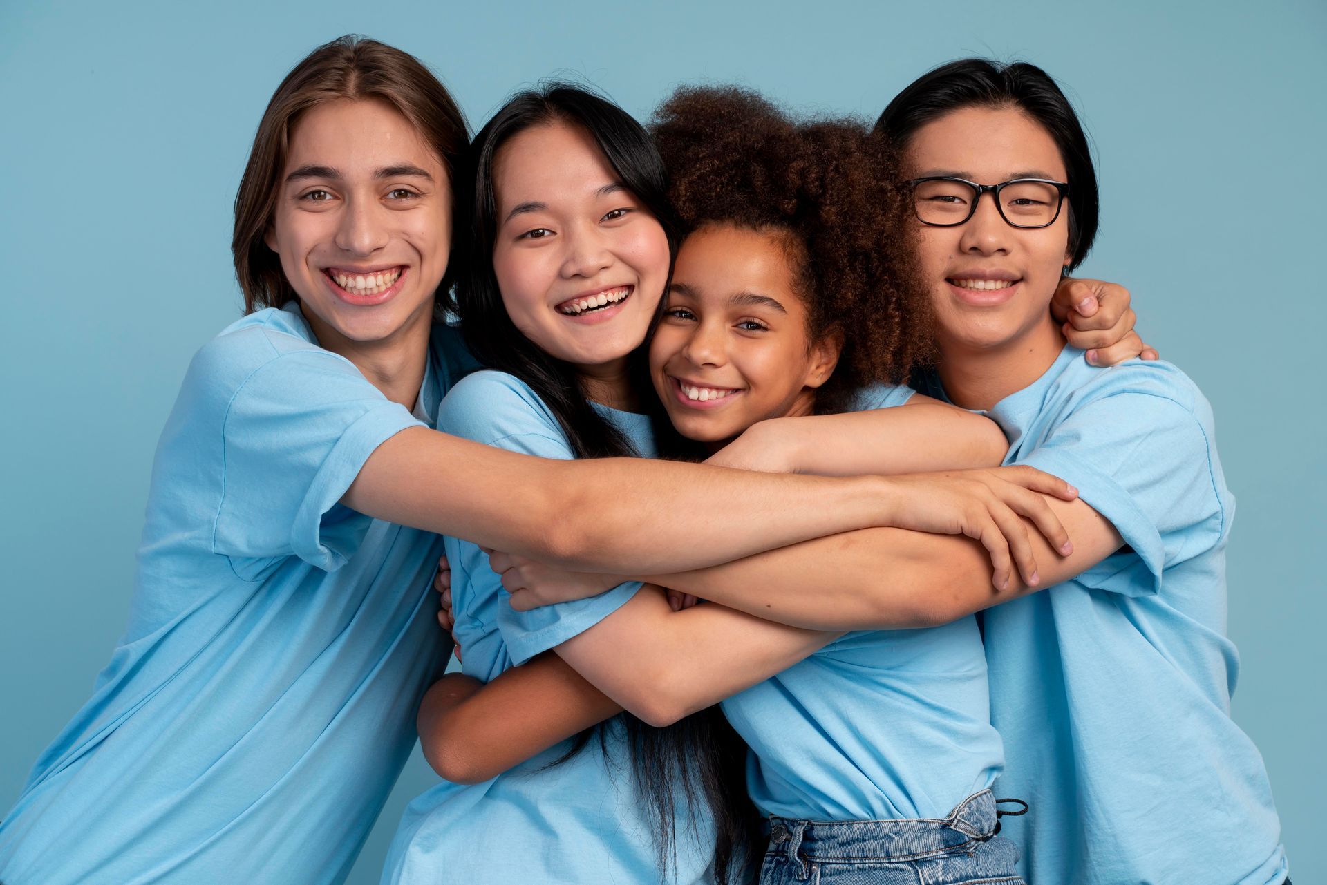 Vier Personen in blauen Hemden umarmen sich und lächeln vor einem blauen Hintergrund.
