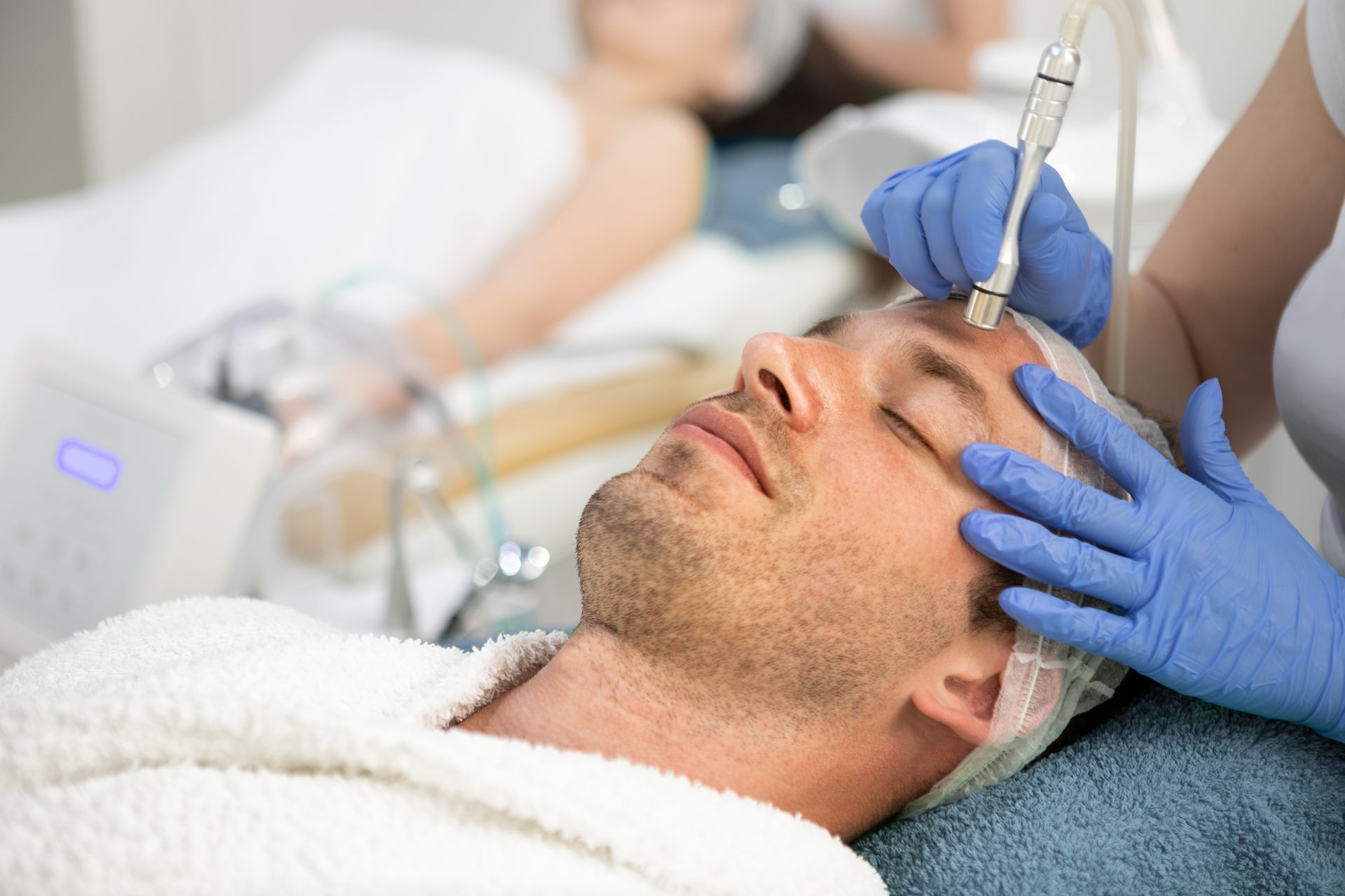 Man receiving facial treatment with a handheld device at a spa.