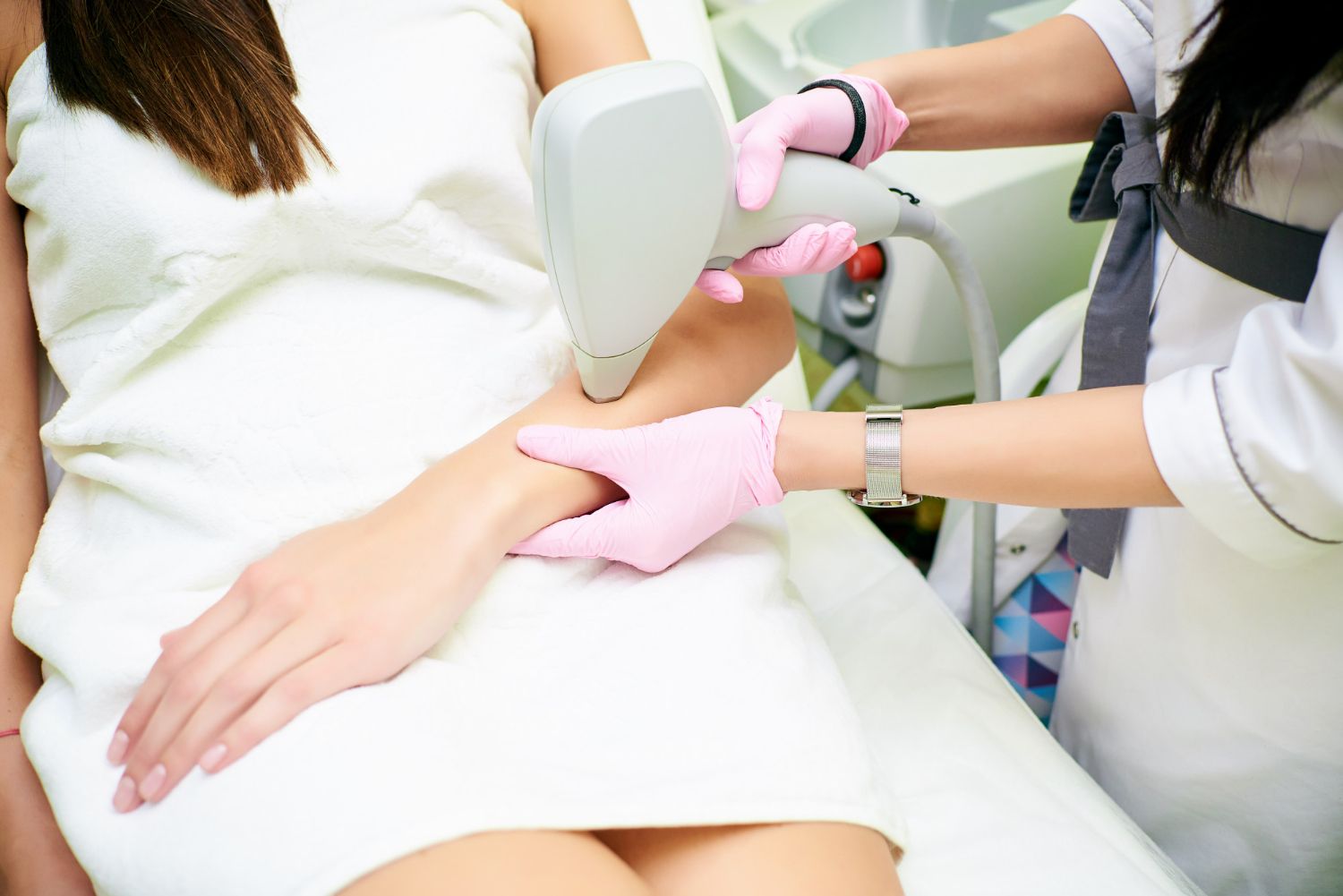 Cosmetic treatment on a woman’s thigh with a handheld device and gloved technician hands