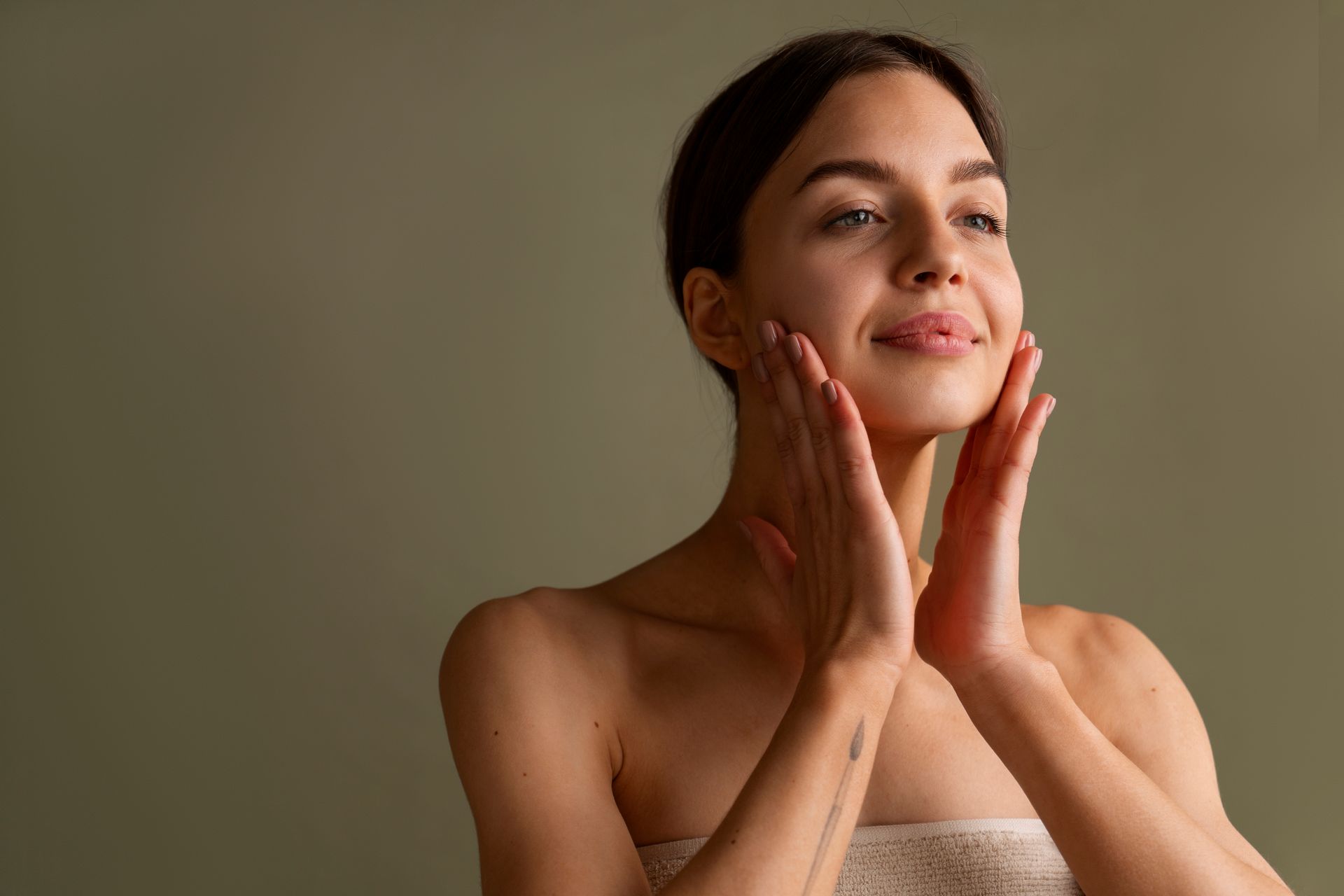 A woman is touching her face with her hands and smiling.