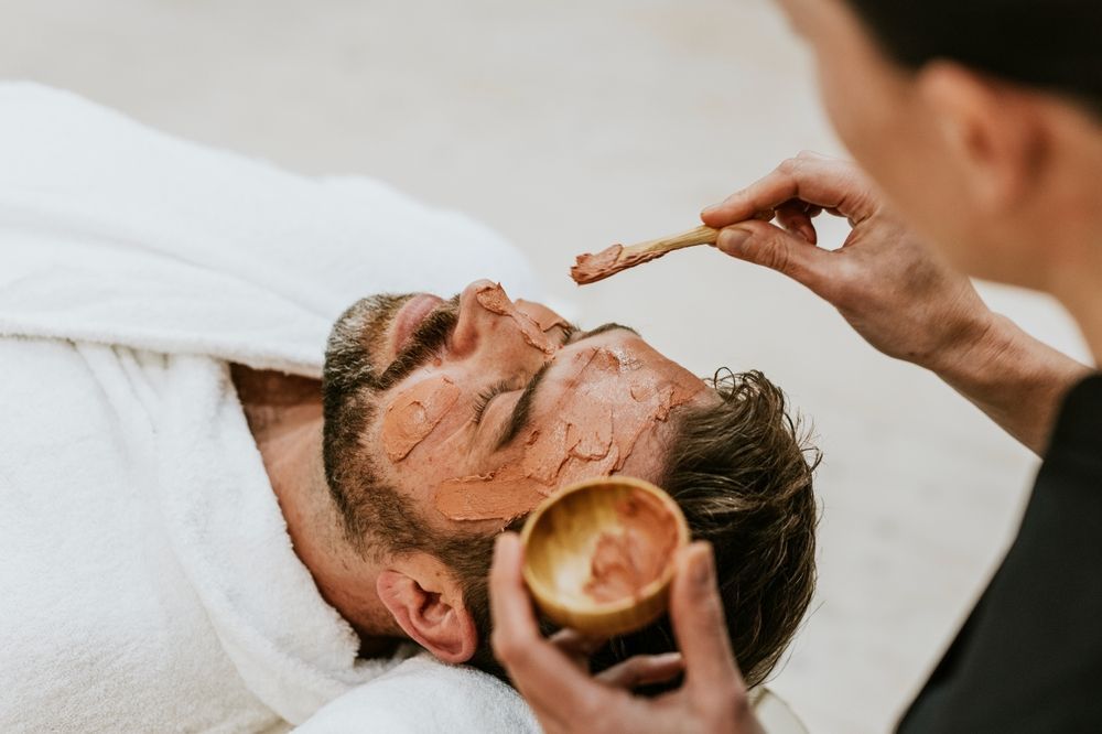 Man receiving a facial treatment while a beautician applies product to his face