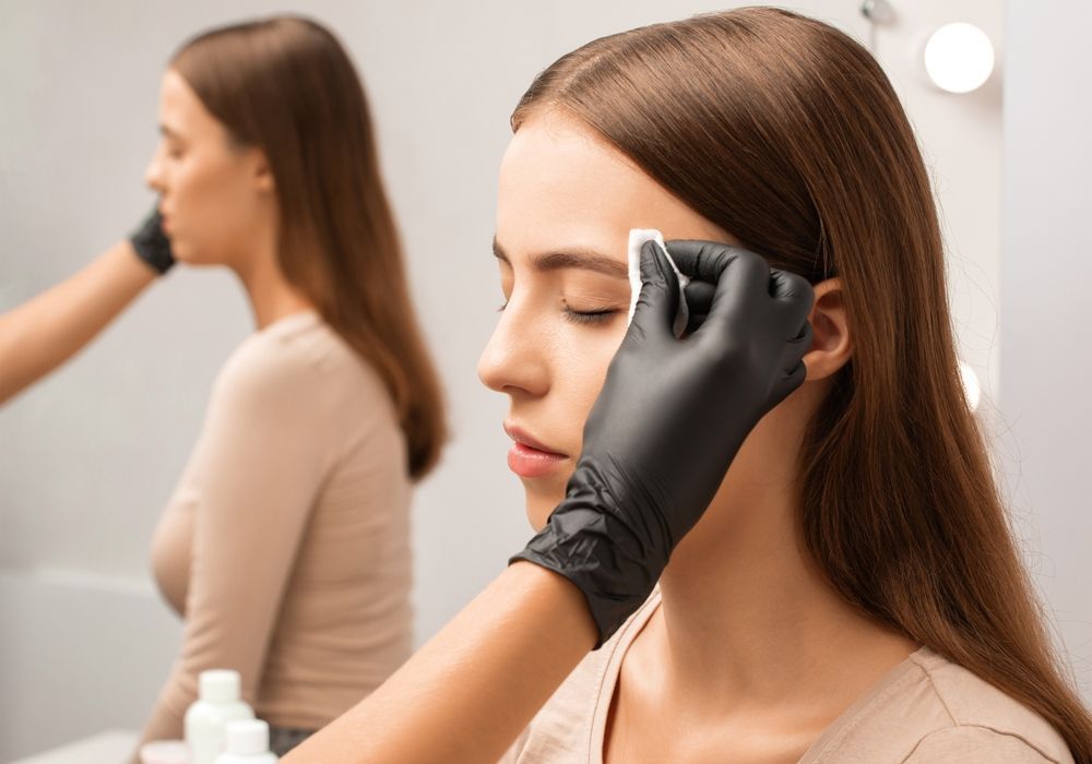 Cosmetologist applying eyeliner to a seated client in a salon mirror view