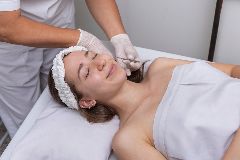 Spa therapist giving a facial massage to a reclining client in a white towel and headband