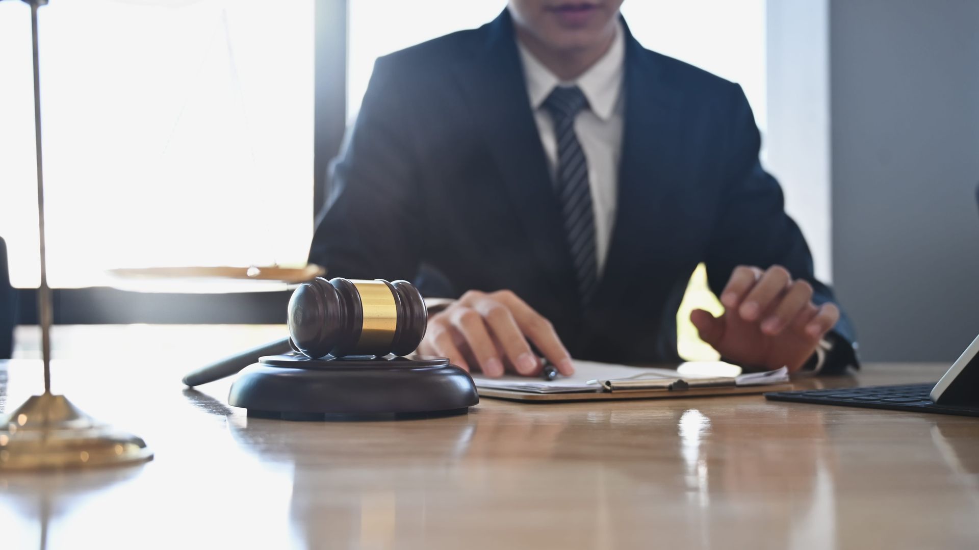 Businessperson in a suit signing papers beside a gavel at a desk in an office