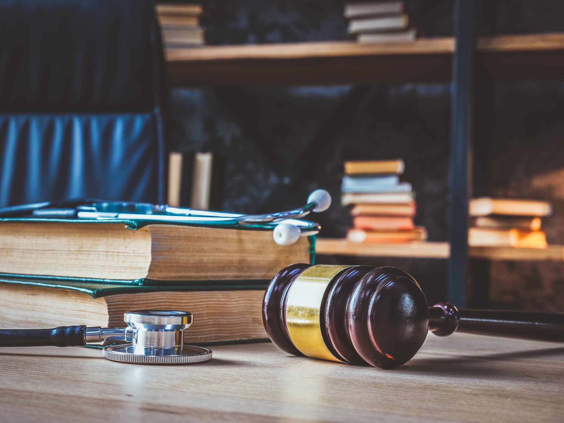 Gavel next to stethoscope on a desk with medical books and a bookshelf in the background.
