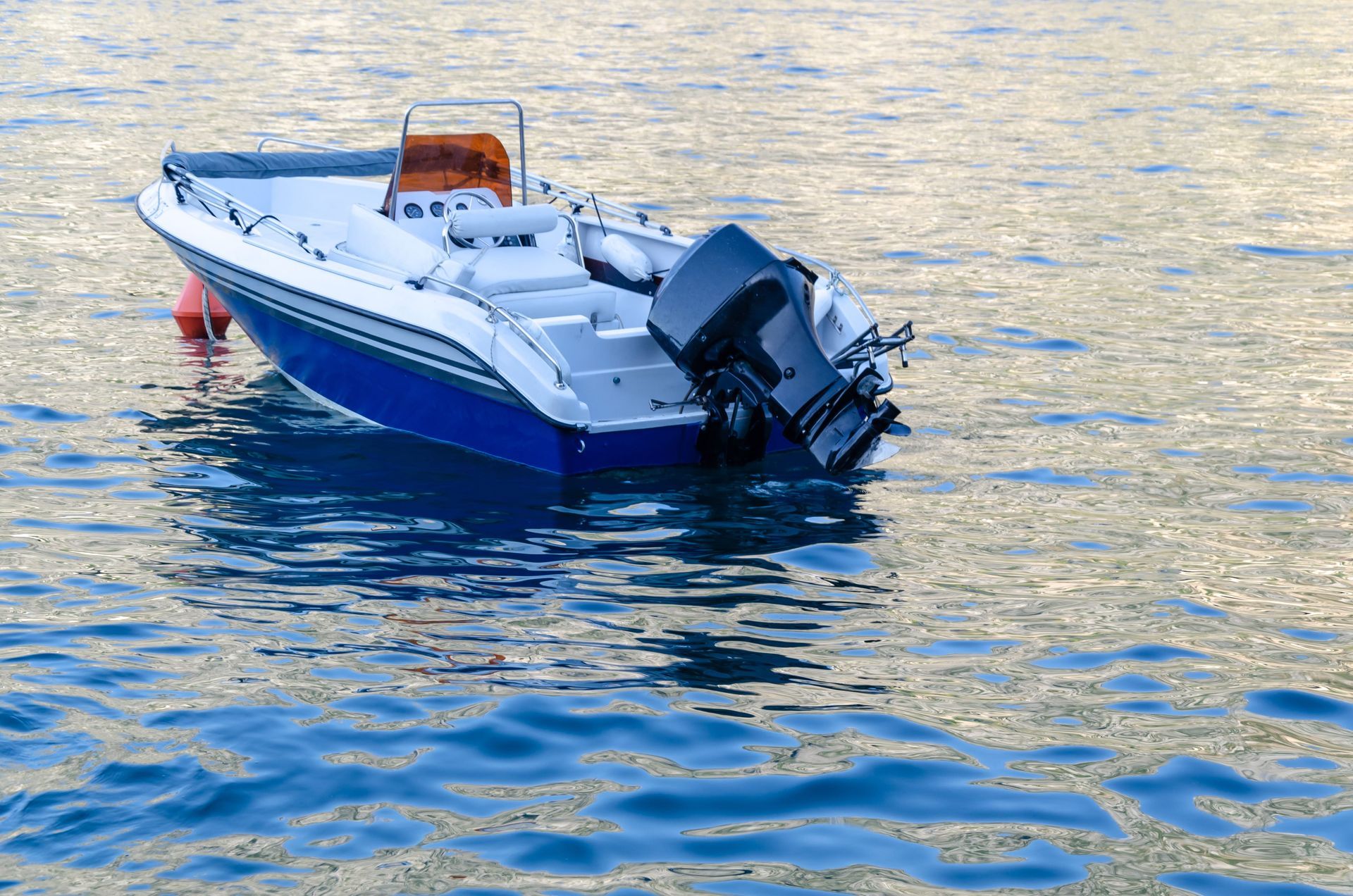 Small white-and-blue motorboat floating on rippling water, with an outboard motor at the stern.