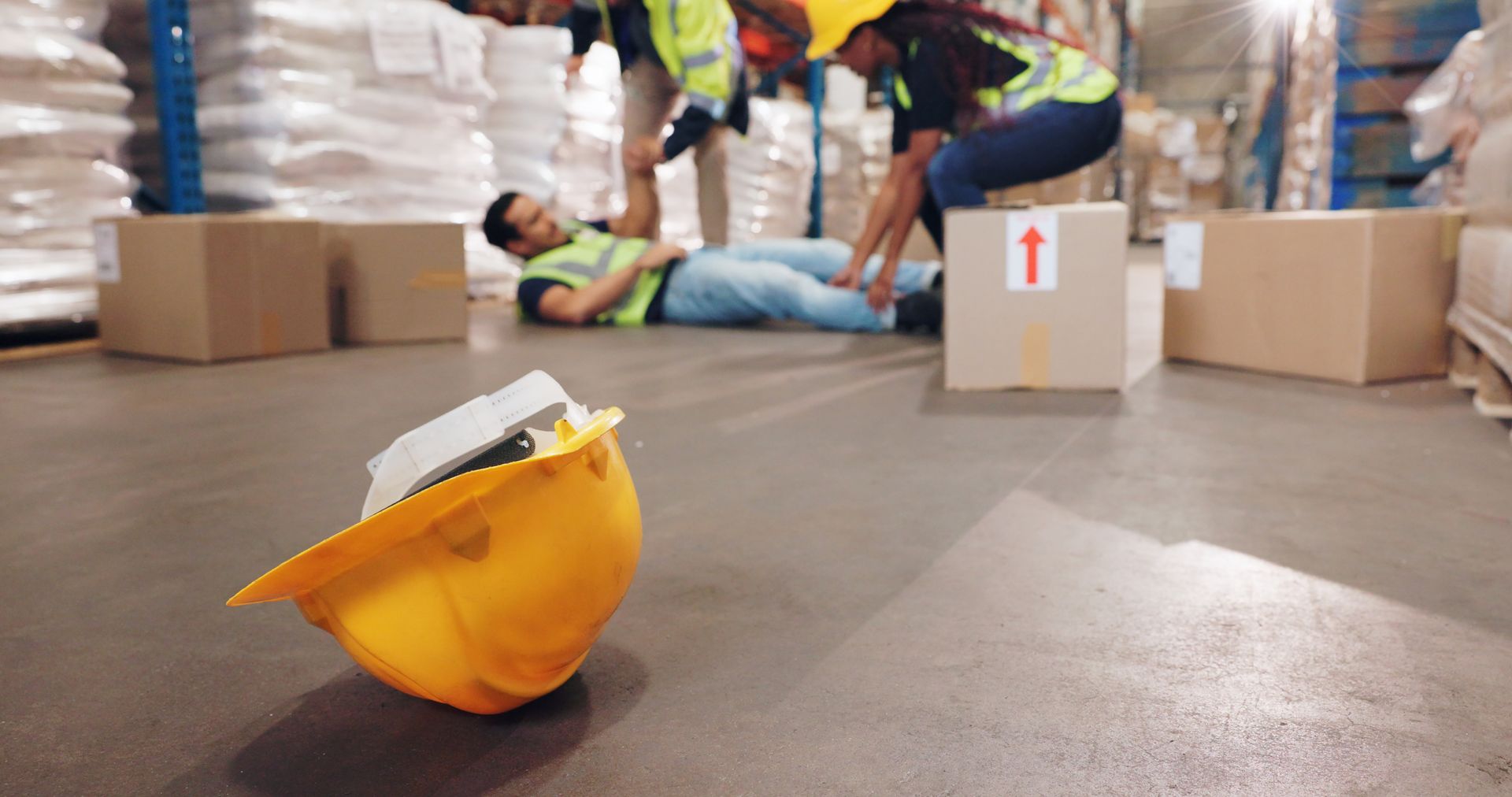 A man is laying on the floor in a warehouse with a hard hat on the floor.