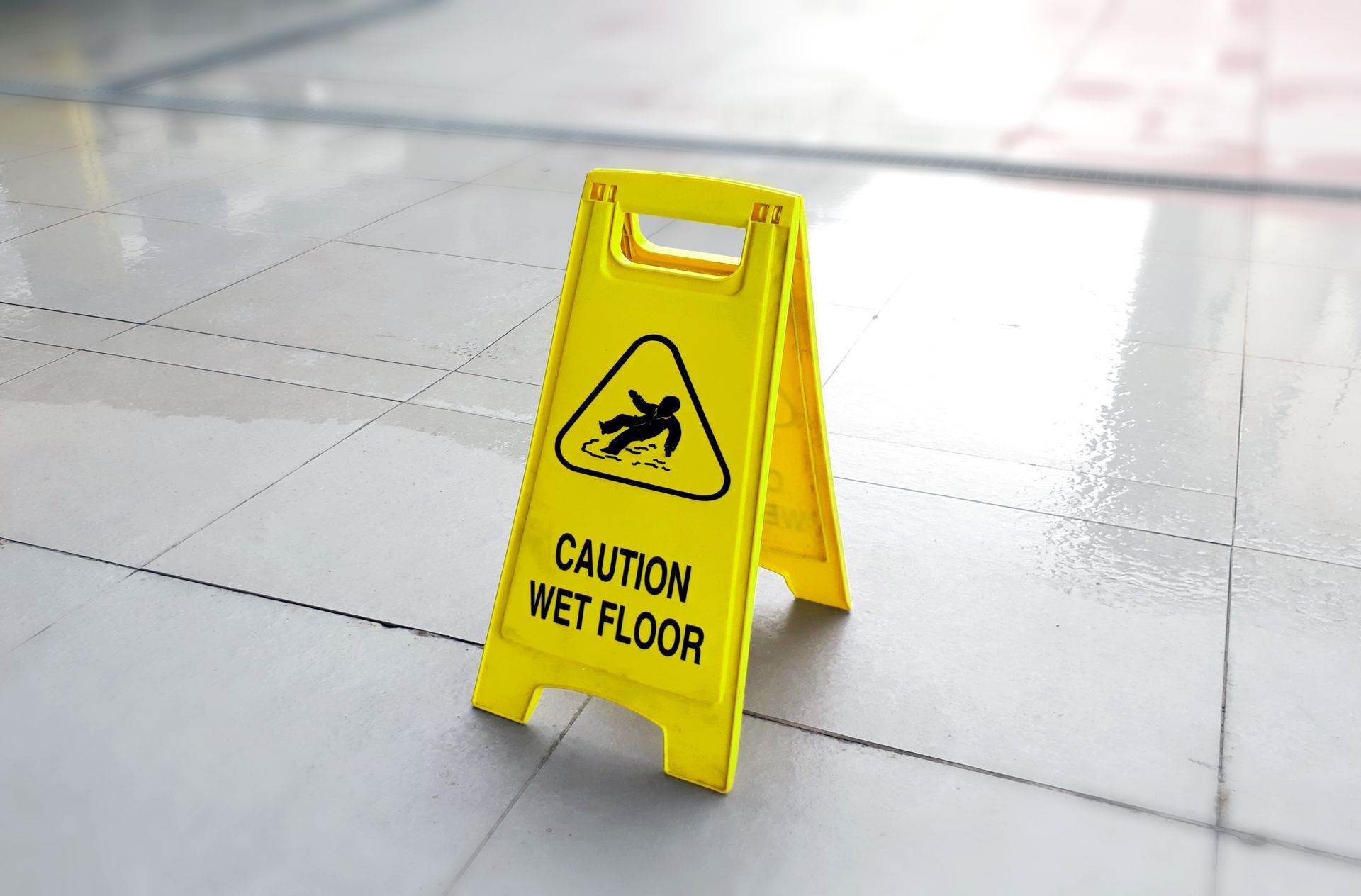 A yellow caution wet floor sign is sitting on a tiled floor.