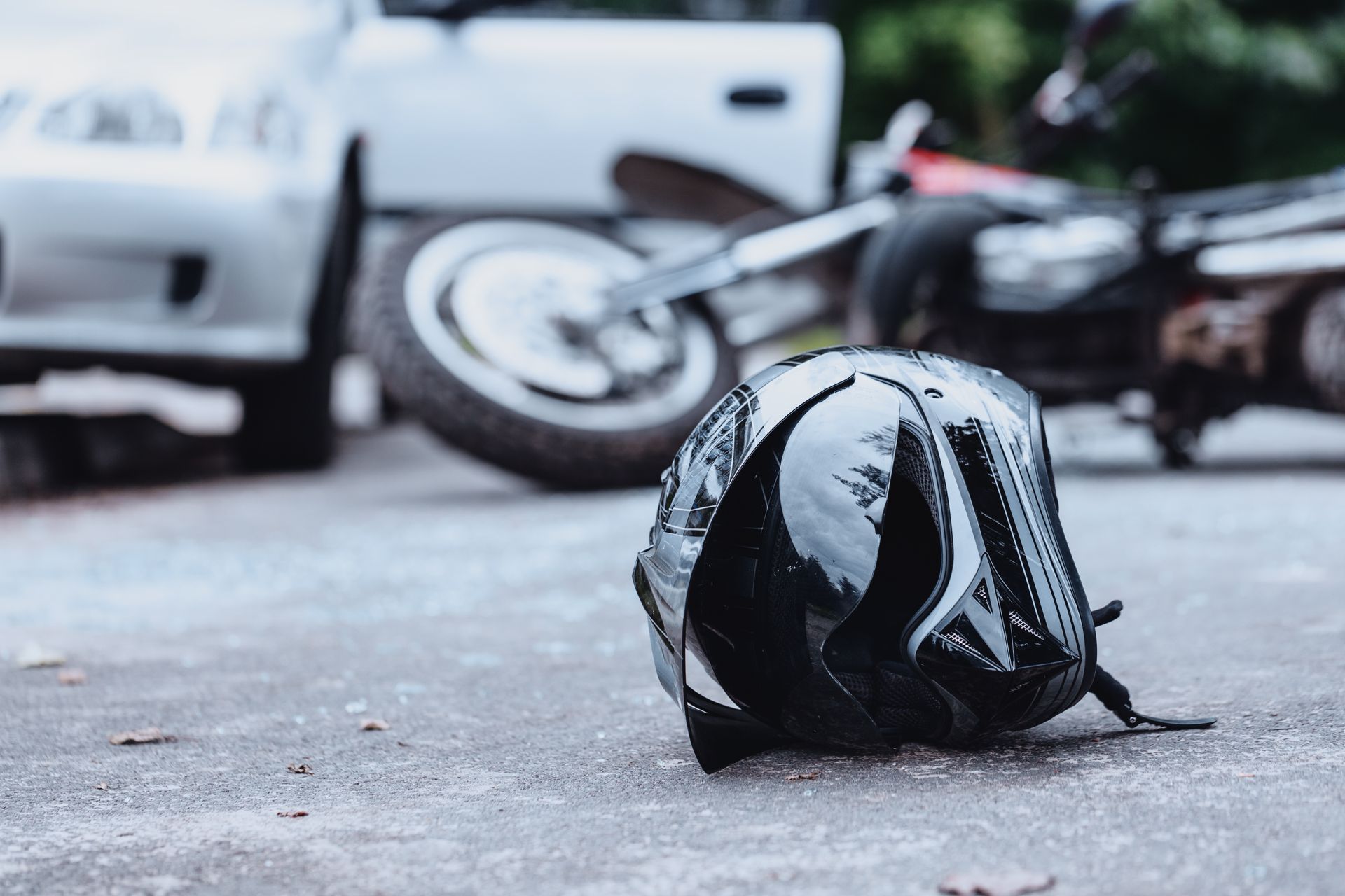 A helmet is laying on the ground in front of a car and motorcycle.