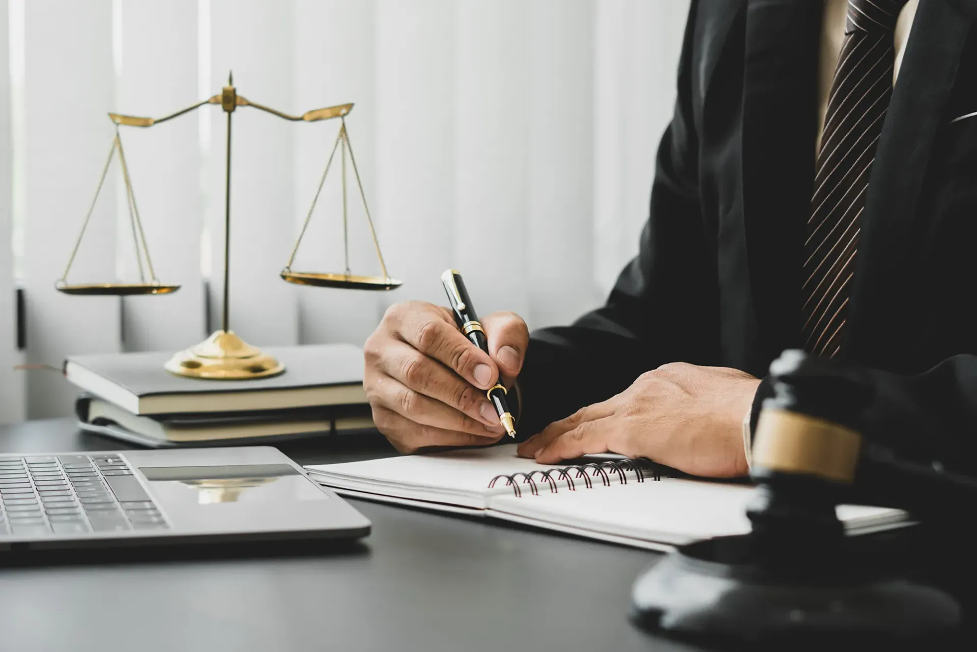 Lawyer writing at desk with scales of justice, laptop, and gavel in office