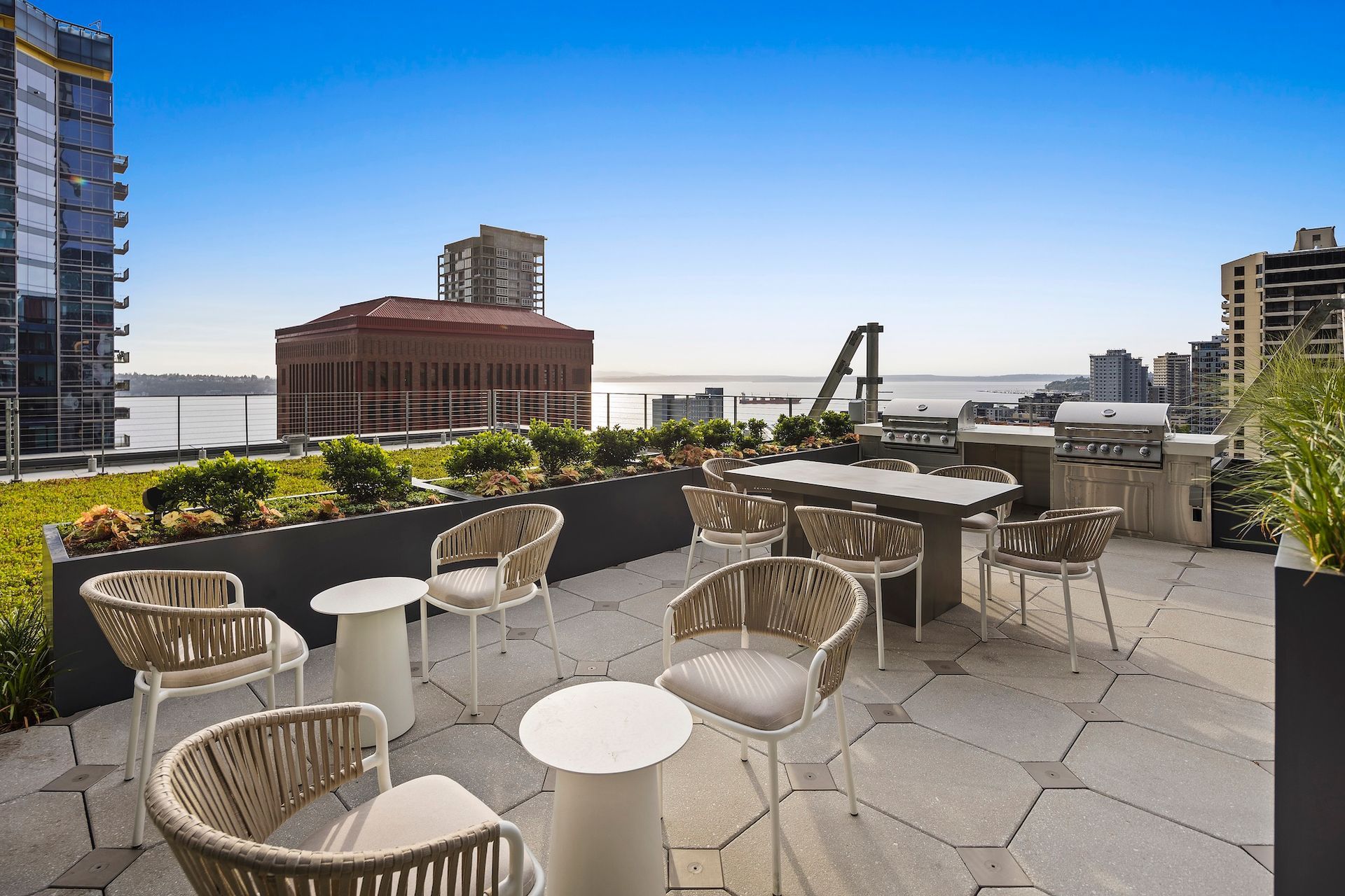 Rooftop patio with wicker chairs, tables, and city skyline under a clear blue sky