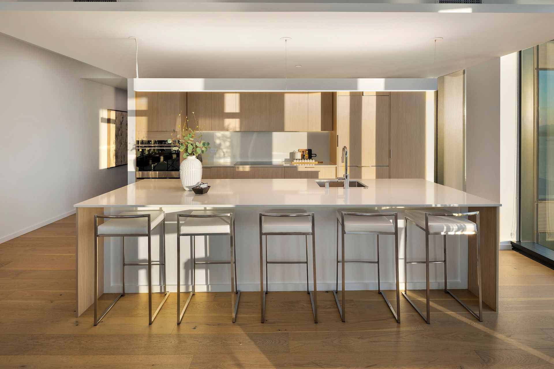 Modern kitchen with a large marble island, bar stools, wood floors, and floor-to-ceiling windows