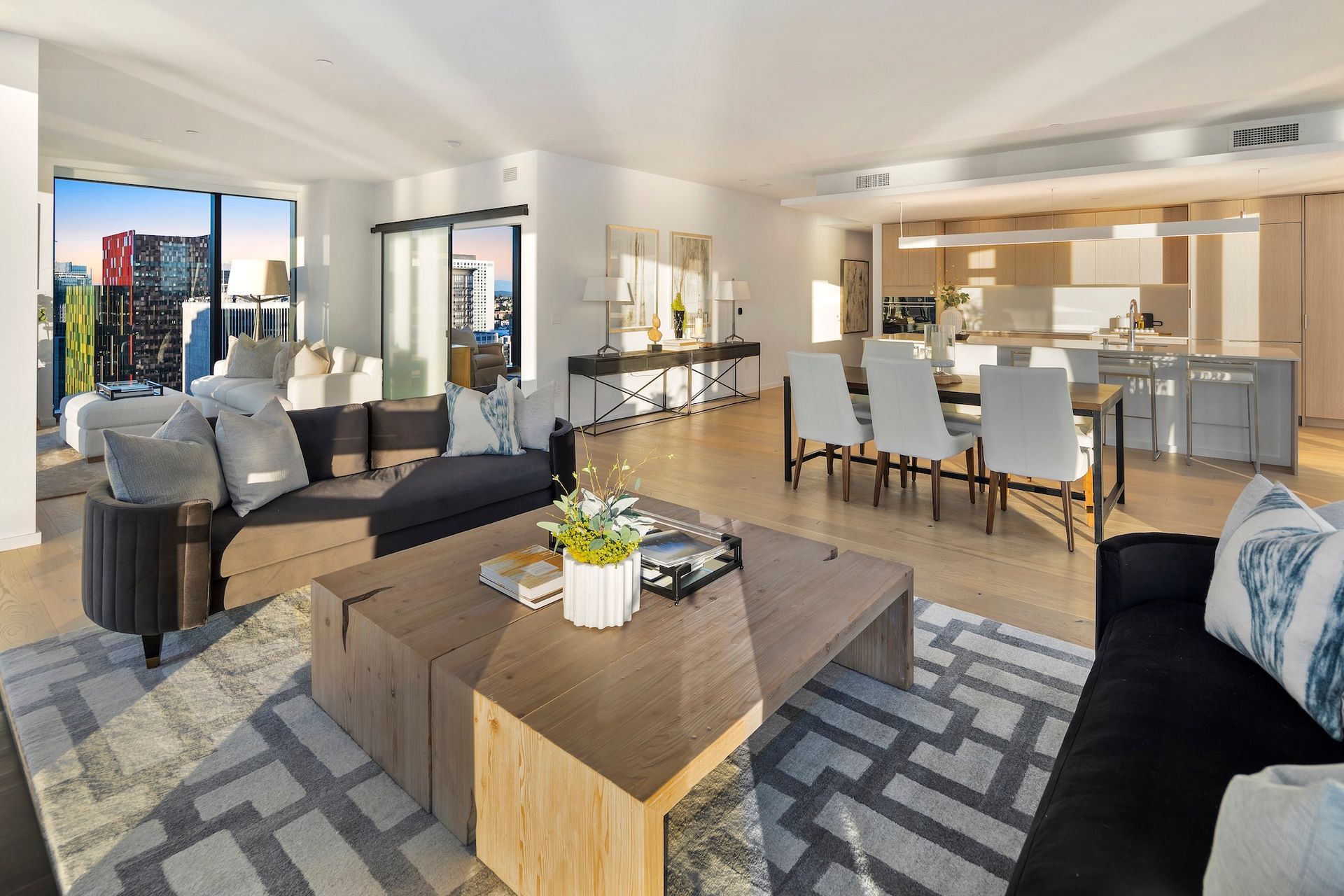 Modern open-concept living room and dining area with gray sofas, coffee table, and bright kitchen beyond