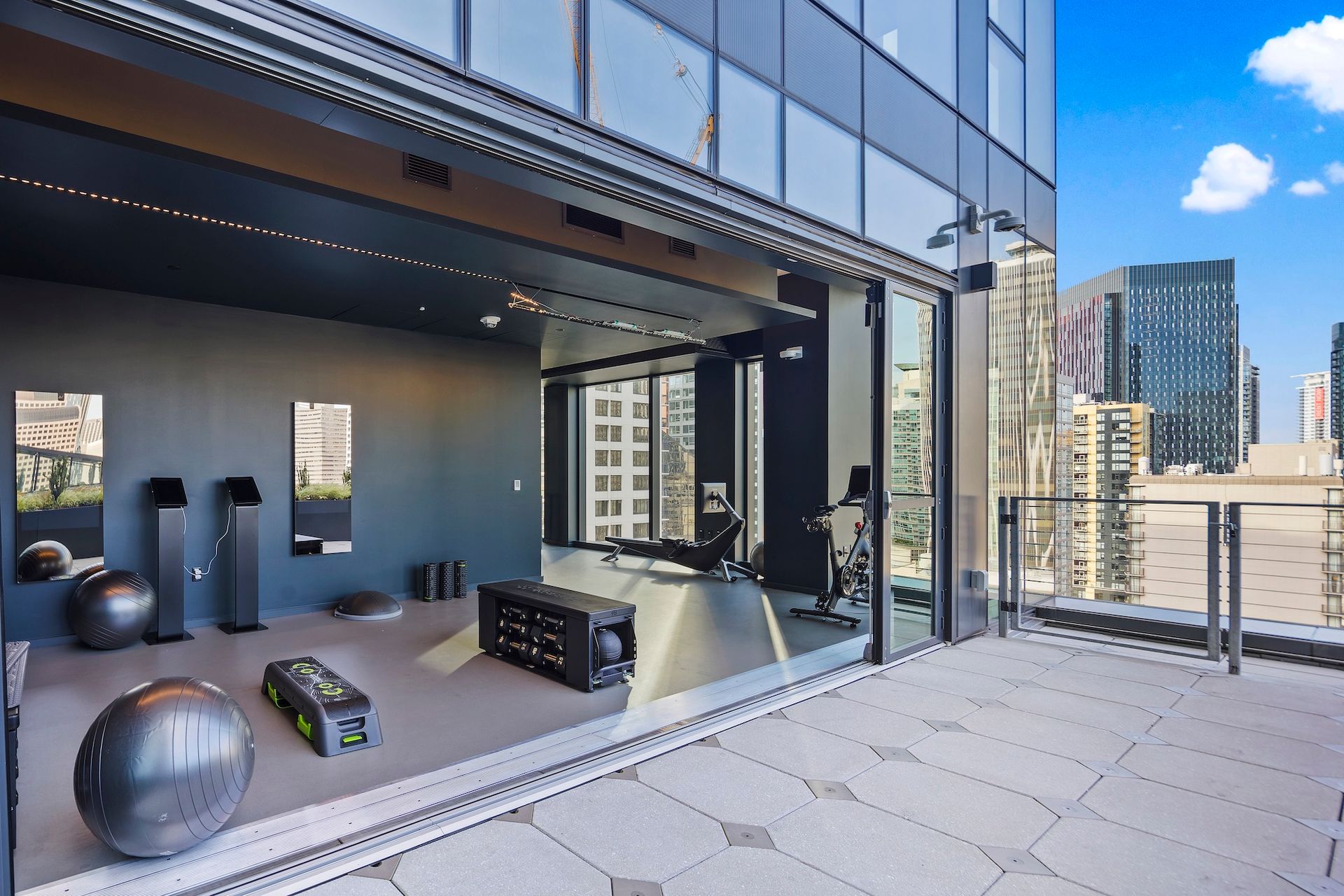 Modern balcony gym with workout equipment, city skyline, and blue sky view