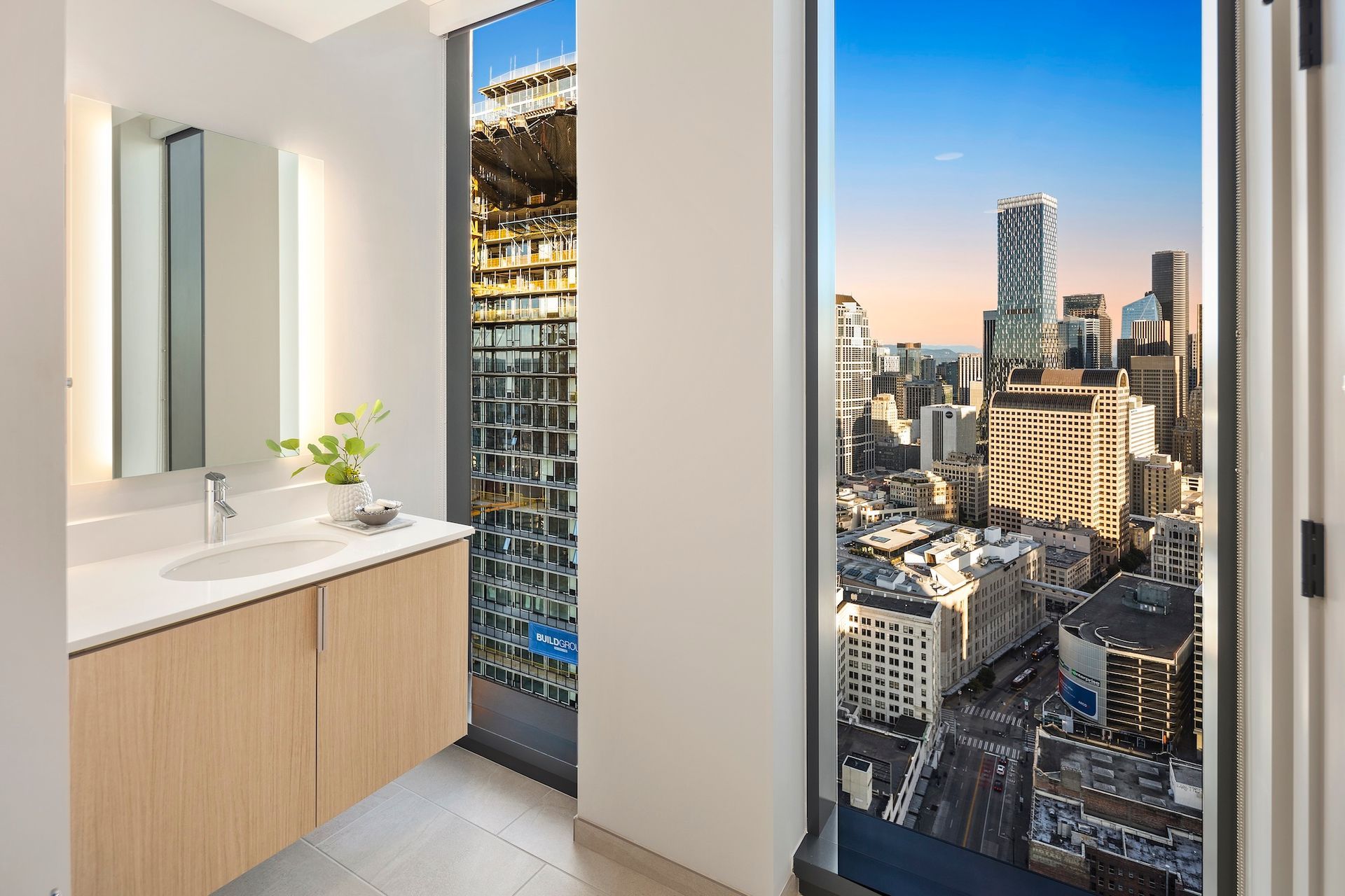 Modern bathroom with vanity and mirror beside floor-to-ceiling windows overlooking a city skyline