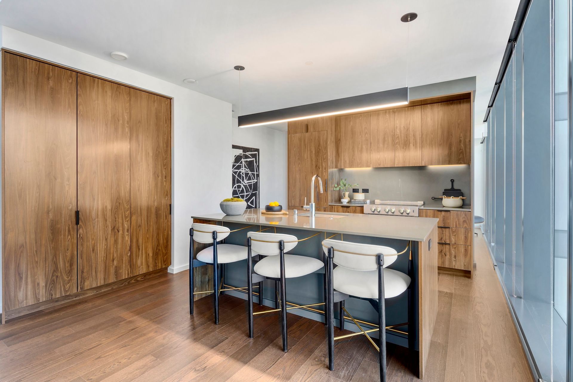 Modern kitchen with island, bar stools, wood cabinets, and blue glass doors