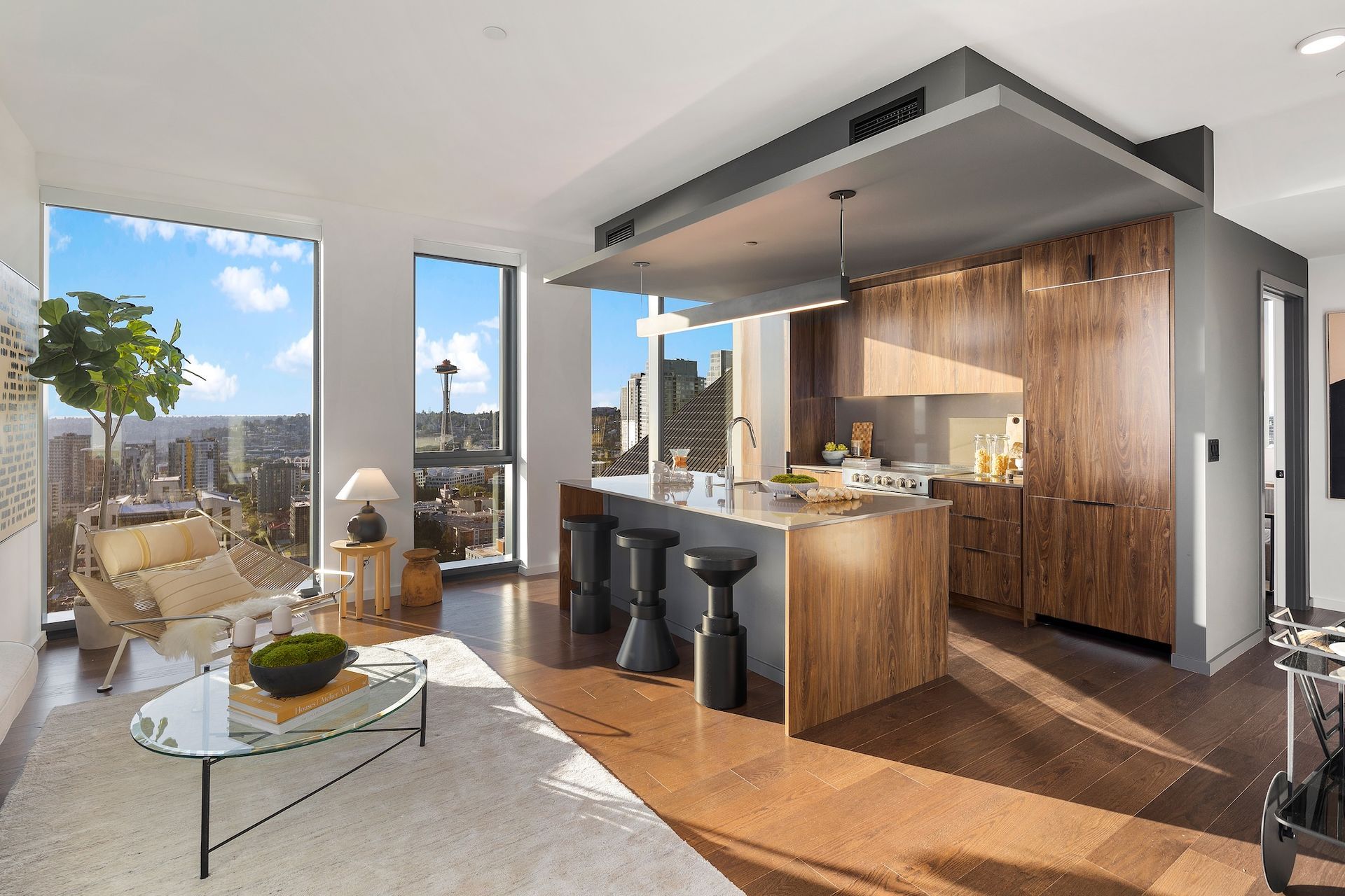 Modern loft kitchen and living room with wood accents, bar stools, and city view through floor-to-ceiling windows