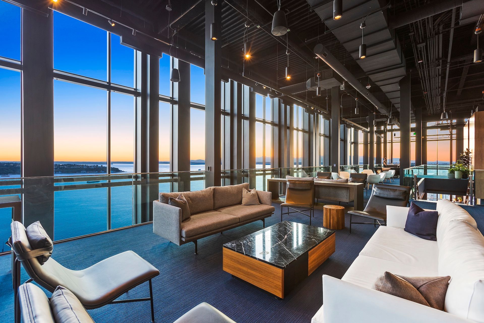 Modern lounge with floor-to-ceiling windows overlooking water at sunset