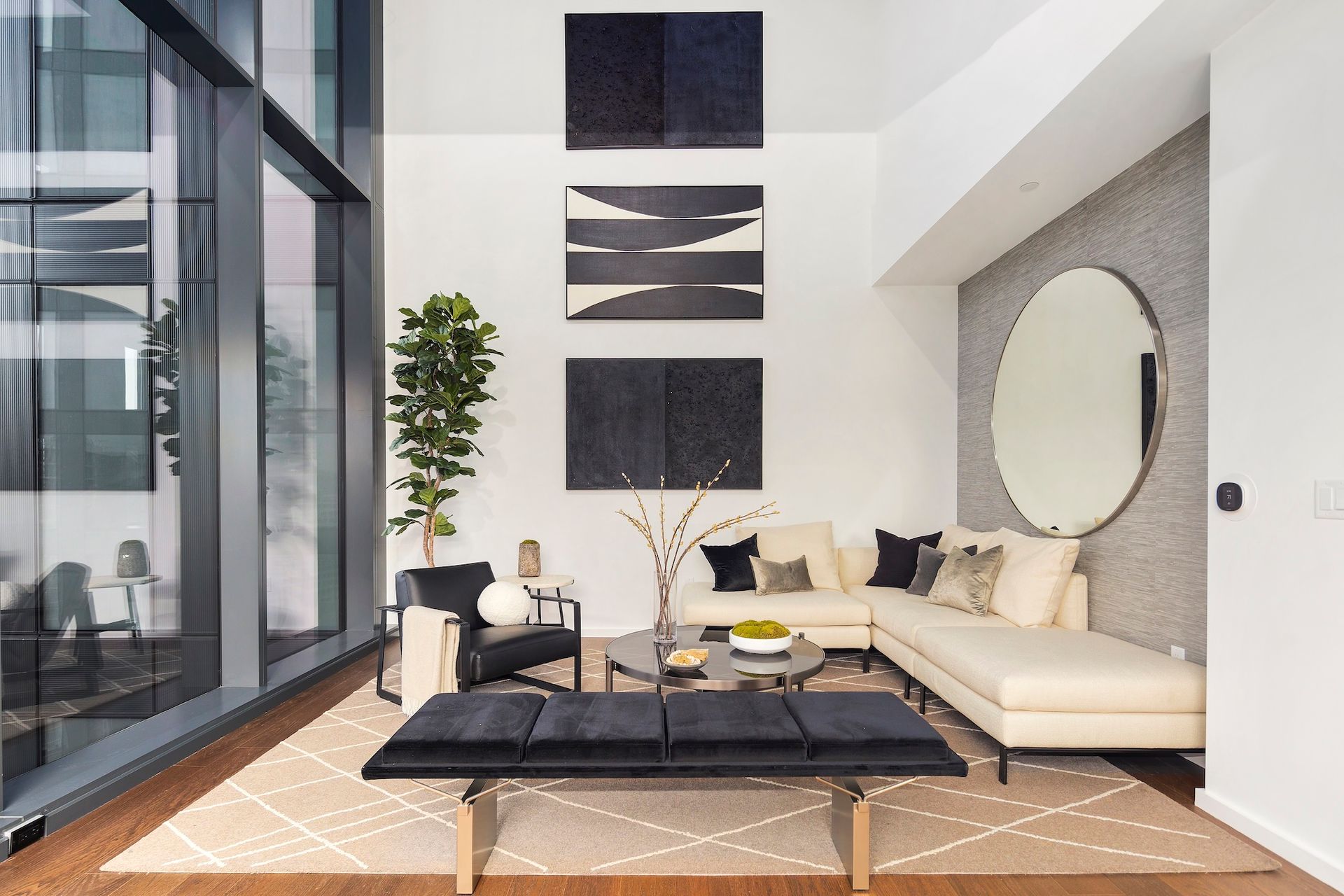 Modern living room with cream sectional, black coffee table, wall art, and large glass windows