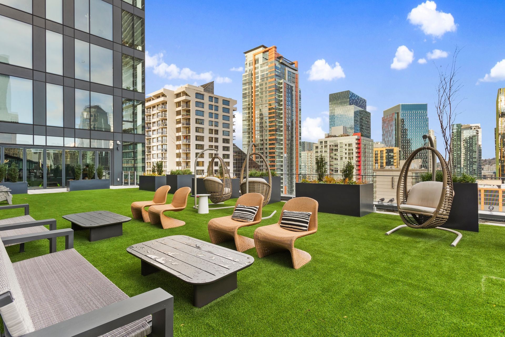 Rooftop terrace with lounge chairs, green turf, and city skyline under a blue sky