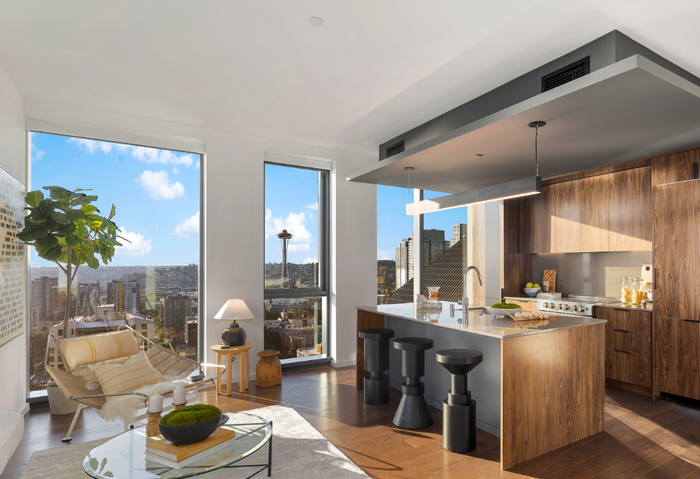 Modern apartment living room and kitchen with city views, wood accents, and a cozy lounge chair by the window.