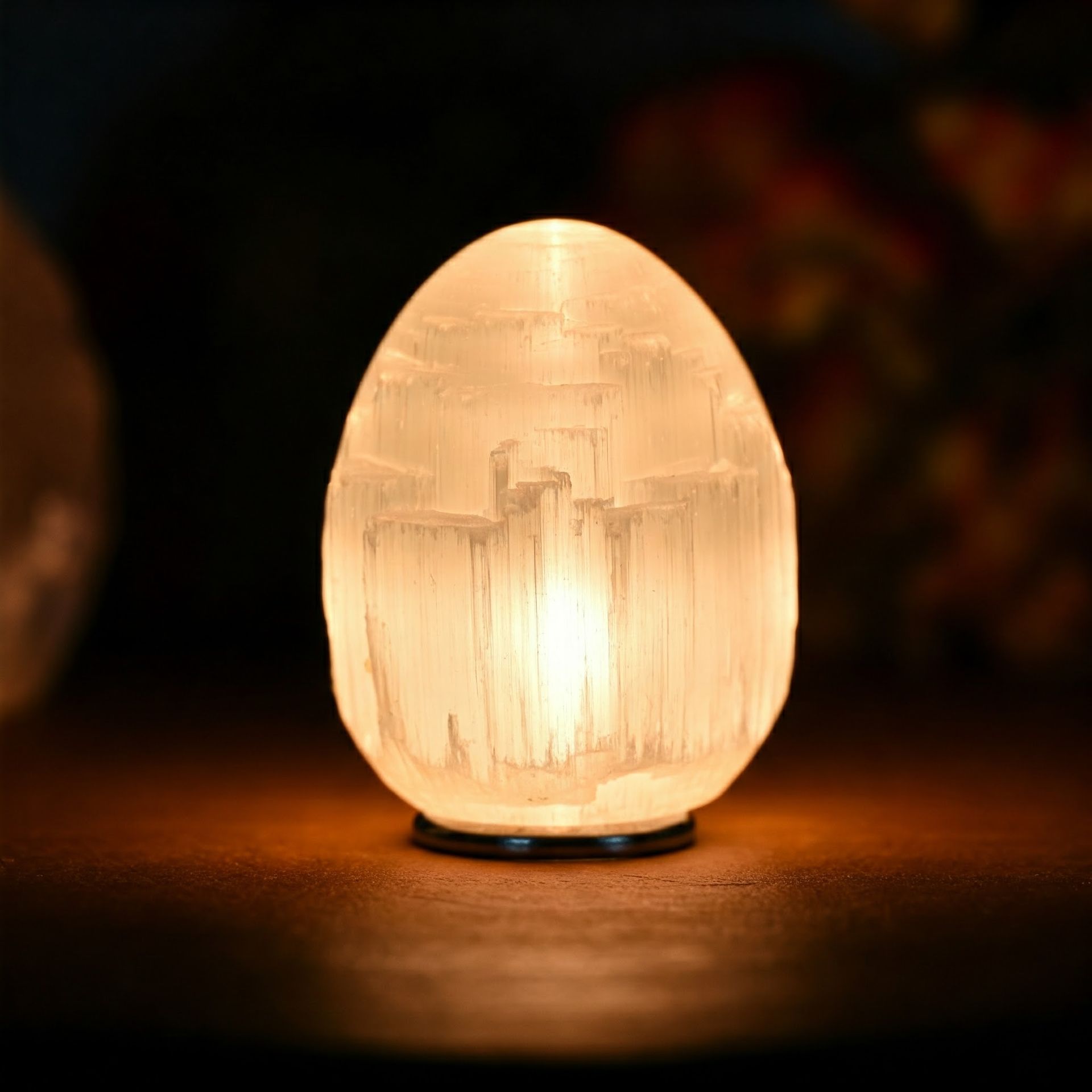 Glowing white selenite egg-shaped lamp on a dark wooden surface, emitting a soft, warm light.