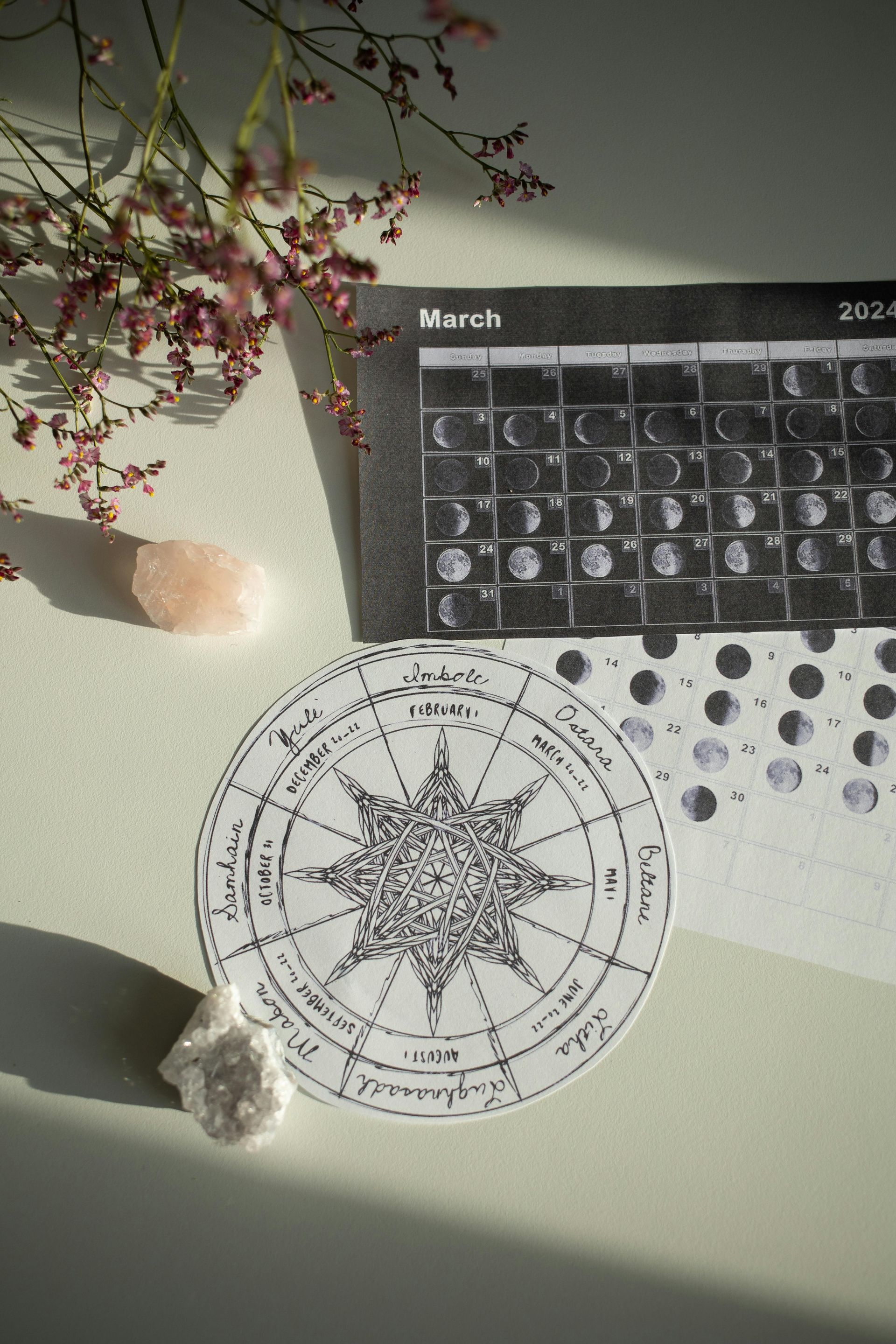 Astrology-themed scene with a moon phase calendar, star map, crystals, and pink flowers.