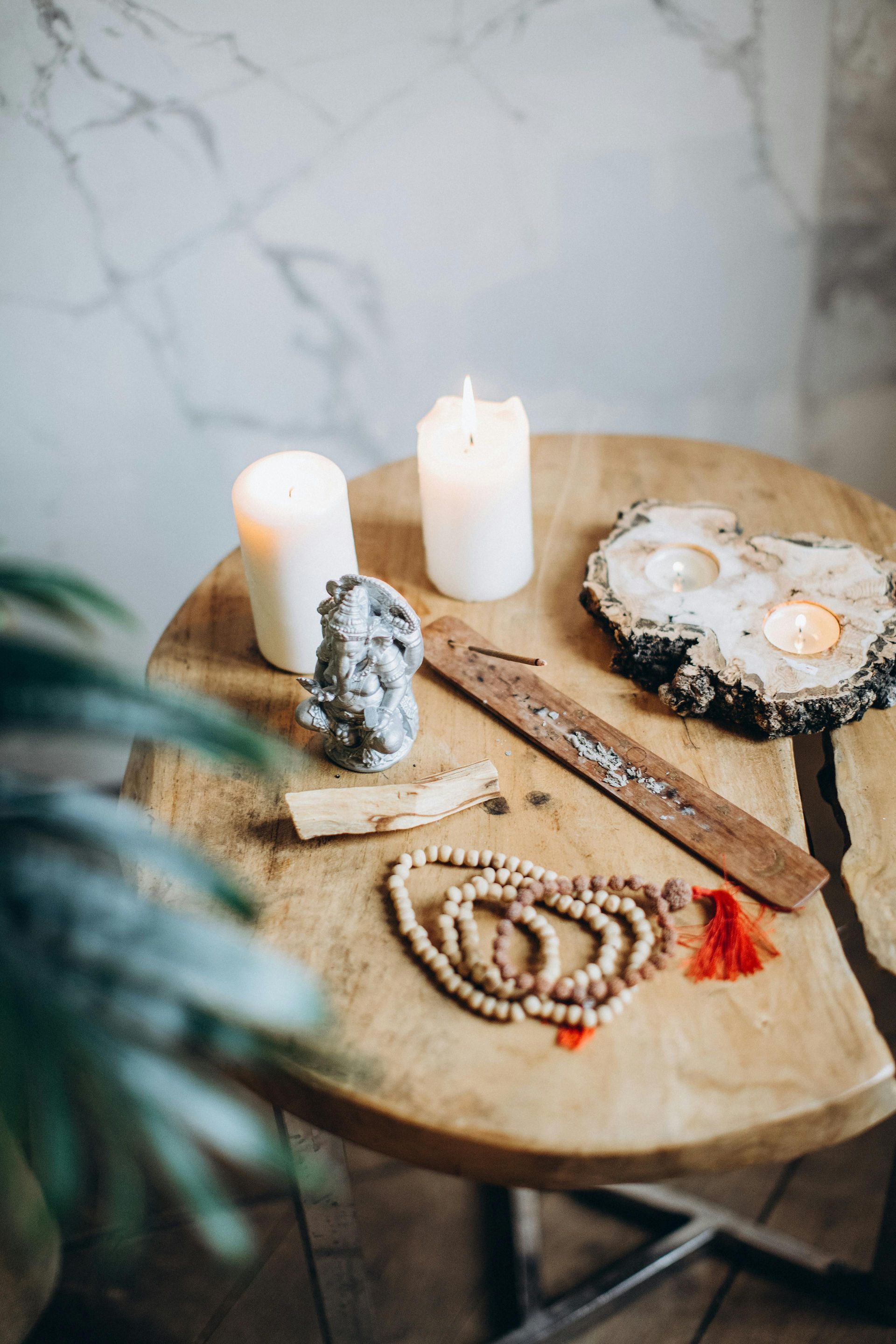 A wooden table with candles , beads , and a plant on it.